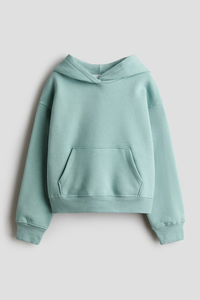 Ein locker geschnittener Hoodie in MintgrÃ¼n ist von vorne zu sehen und zeigt eine gefÃ¼tterte Kapuze mit Wickel-Front-Detail sowie Ã¼berschnittene Schultern. Das Design verfÃ¼gt Ã¼ber eine KÃ¤ngurutasche auf der Vorderseite und wird mit breiten, gerippten BÃ¼ndchen an den Ãrmeln und am Saum abgerundet. - 1