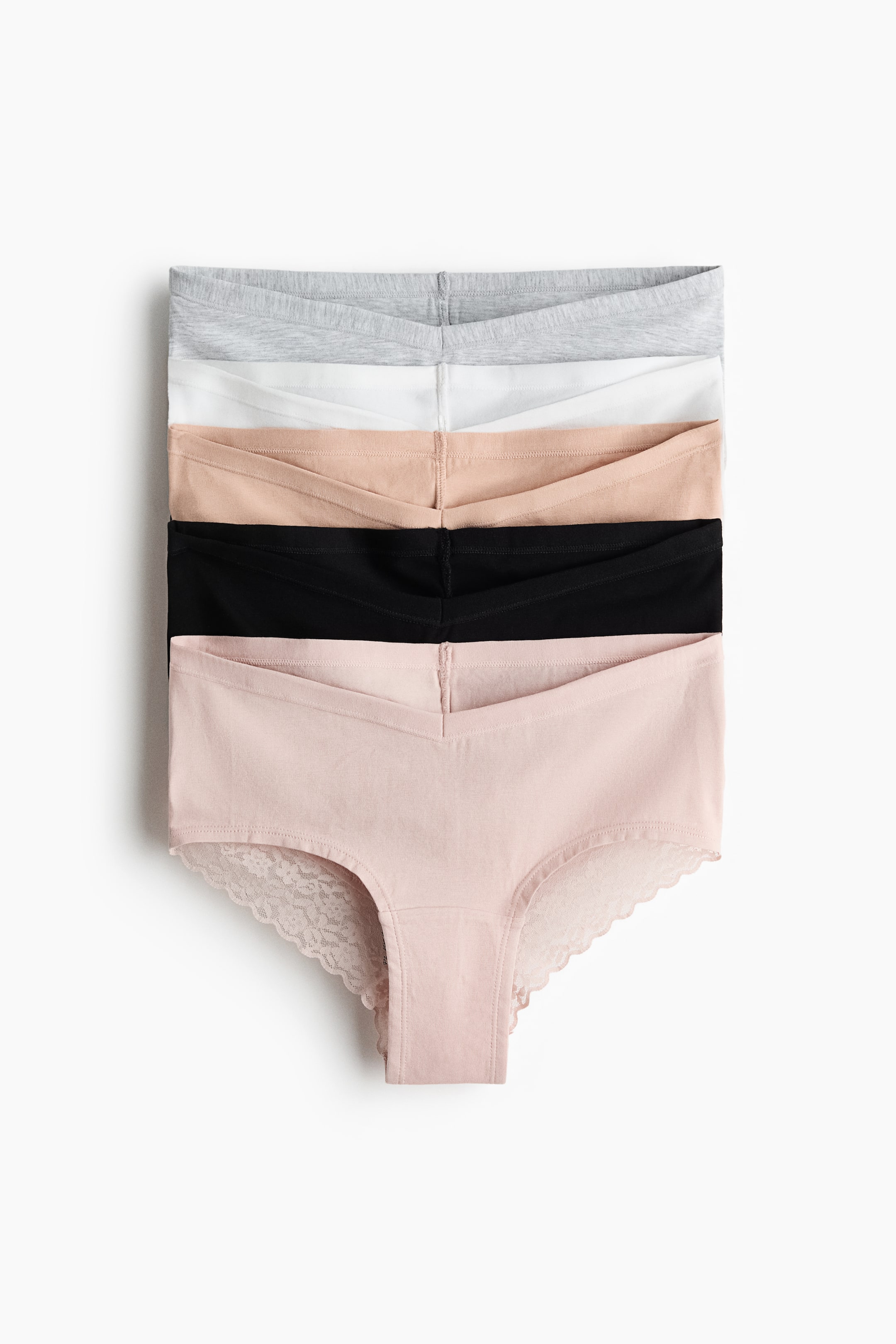 Zobrazit větší obrázek: Pět párů kalhotek z bavlněného džerseje je naskládaných na sebe; shora dolů mají barvy světle šedá, bílá, světle béžová, černá a světle růžová. Každé kalhotky mají nízký pás ve tvaru V na PŘEDNÍ straně a spodní světle růžové kalhotky jsou navíc ozdobeny krajkovanými vroubkovanými lemy podél nohaviček.