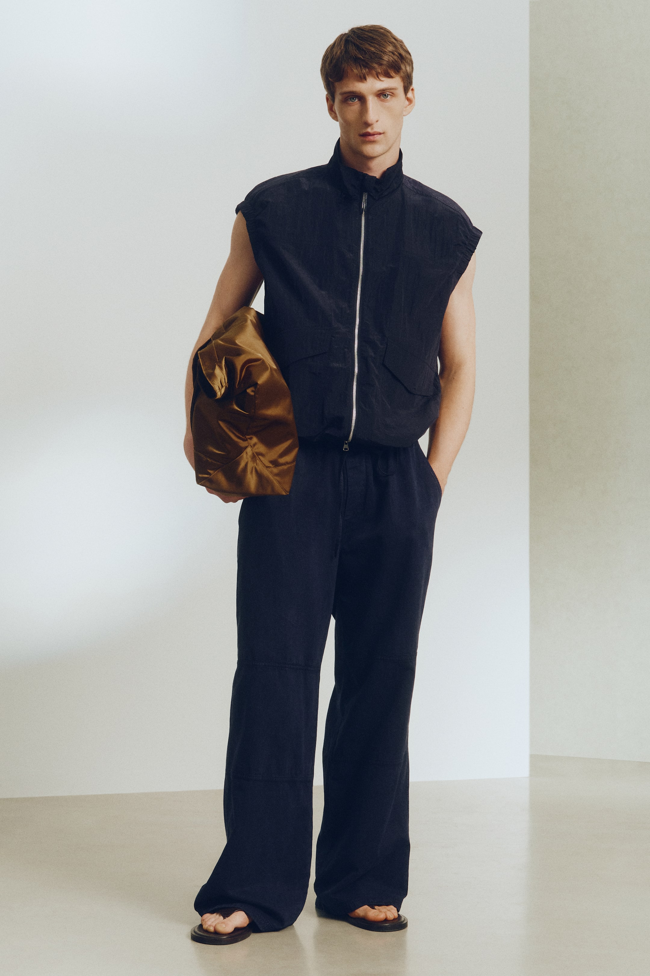 Größeres Bild ansehen: Eine metallisch braune Tasche mit einer geknitterten Textur wird vom Model getragen. Ihre weiche, unstrukturierte Form wird an der Seite des Models gehalten.