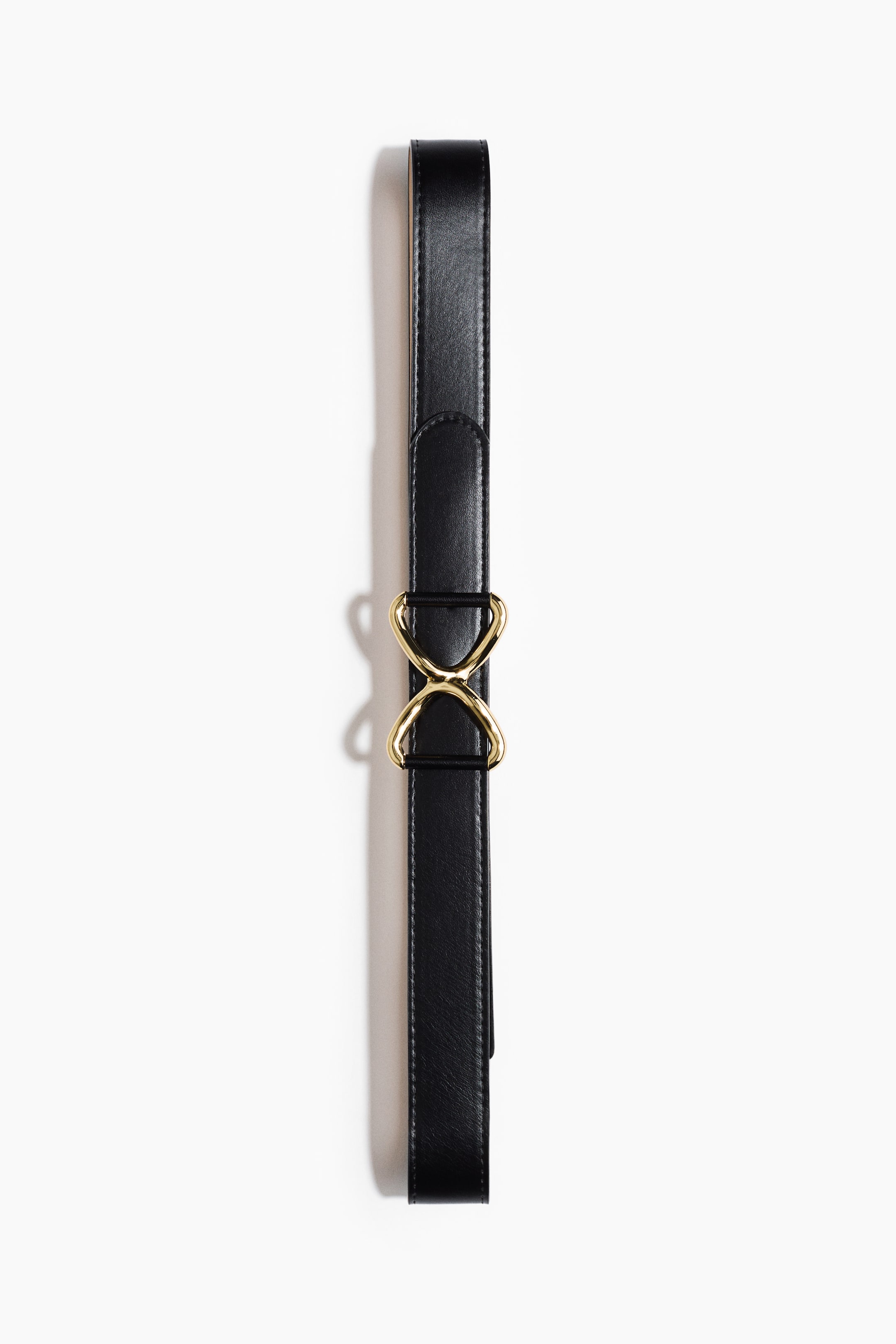 View larger image: A narrow black belt is laying flat, FRONT-facing, featuring a gold-toned metal buckle with an hourglass shape at its center.