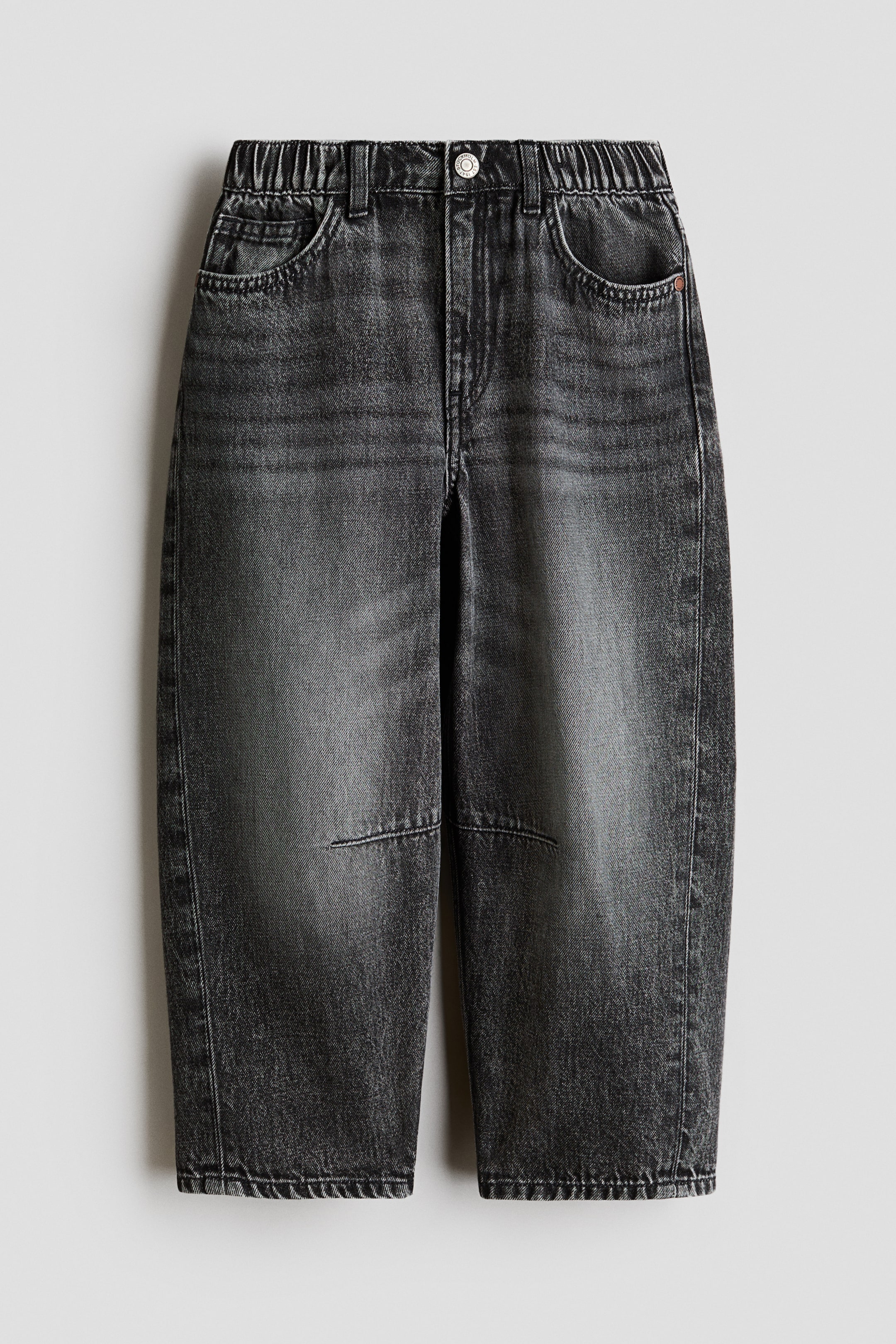 Visa större bild: Svart tvättade denimjeans visas i en framvy, med en elastisk midja med hällor och en enda metallknappstängning. De visar två främre snedställda fickor, en liten myntficka och synliga knälappar på de vida benen, allt med en blekt svart tvätt.