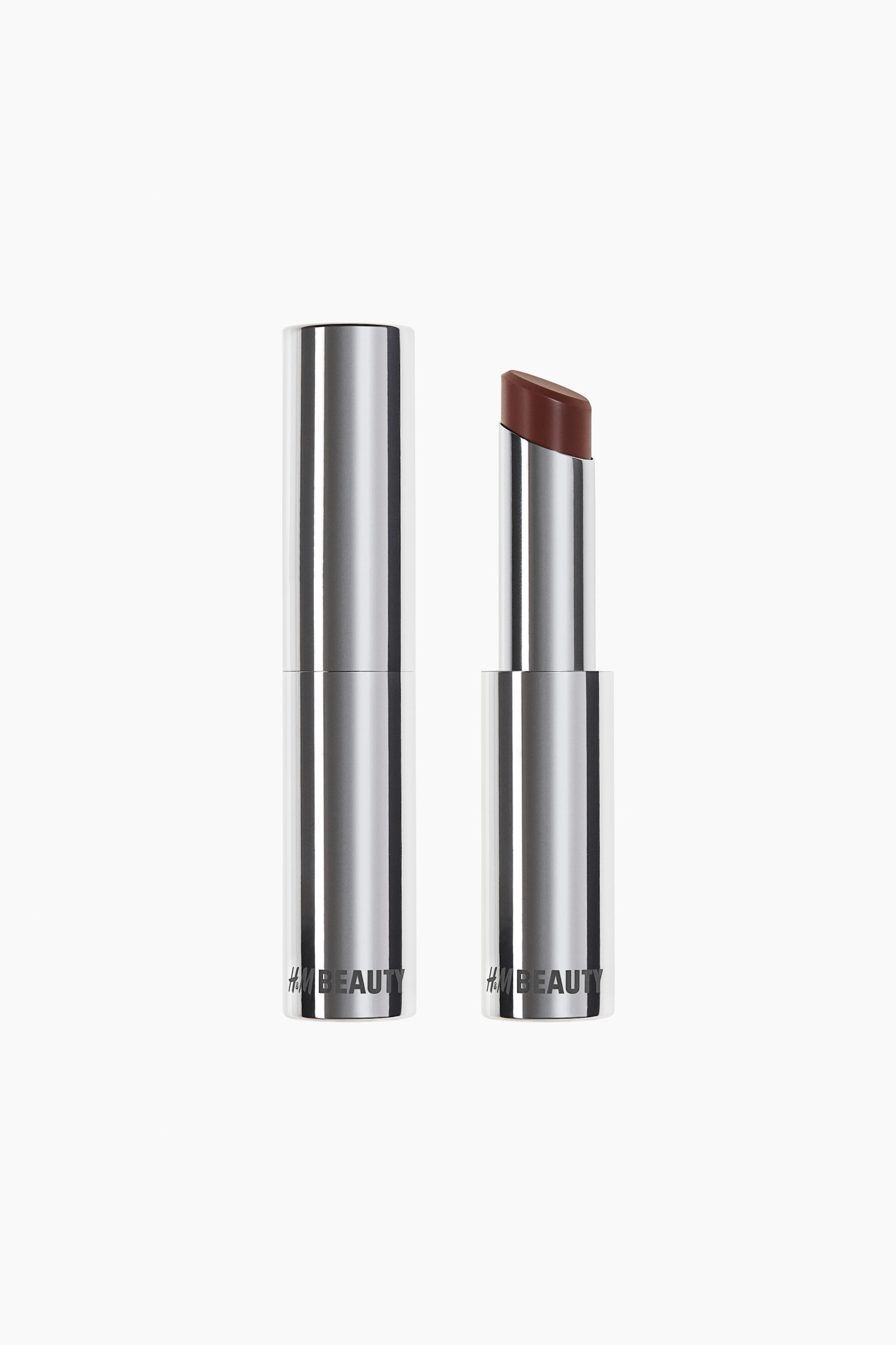 Ver imagem maior: Dois tubos de batom H&M BEAUTY estão de pé, apresentando estojos prateados. Um tubo está fechado e o outro está aberto, exibindo uma bala de batom castanha com uma ponta angulada.