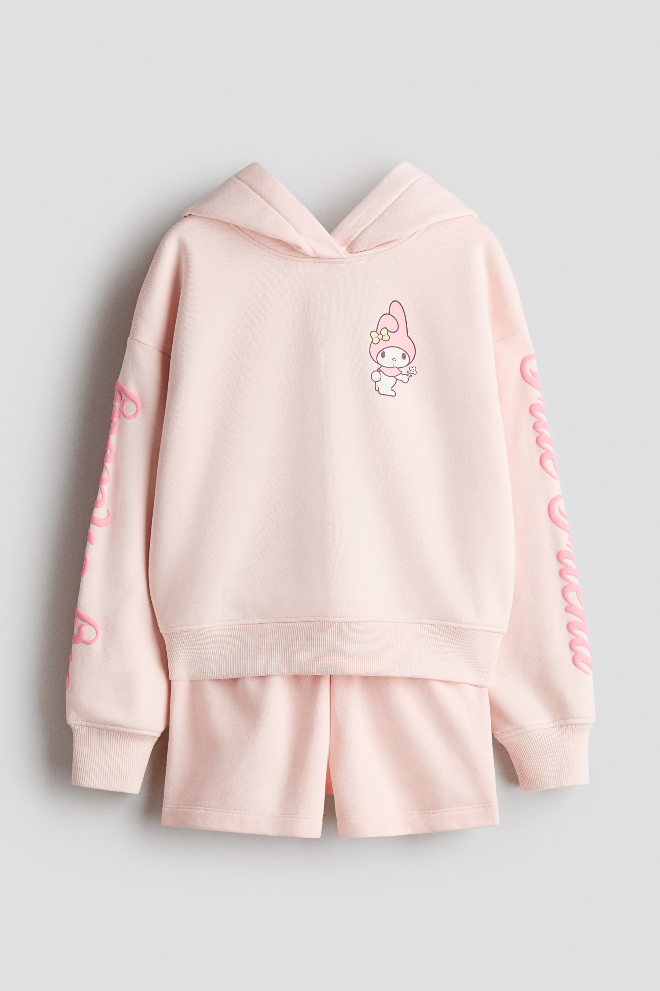 View larger image: A pink hoodie and shorts set is showcased from the front. The hoodie boasts a My Melody character print on the chest, text prints on the sleeves, a wrapover hood, dropped shoulders, and ribbed cuffs and hem. The matching shorts feature an elasticated waist.