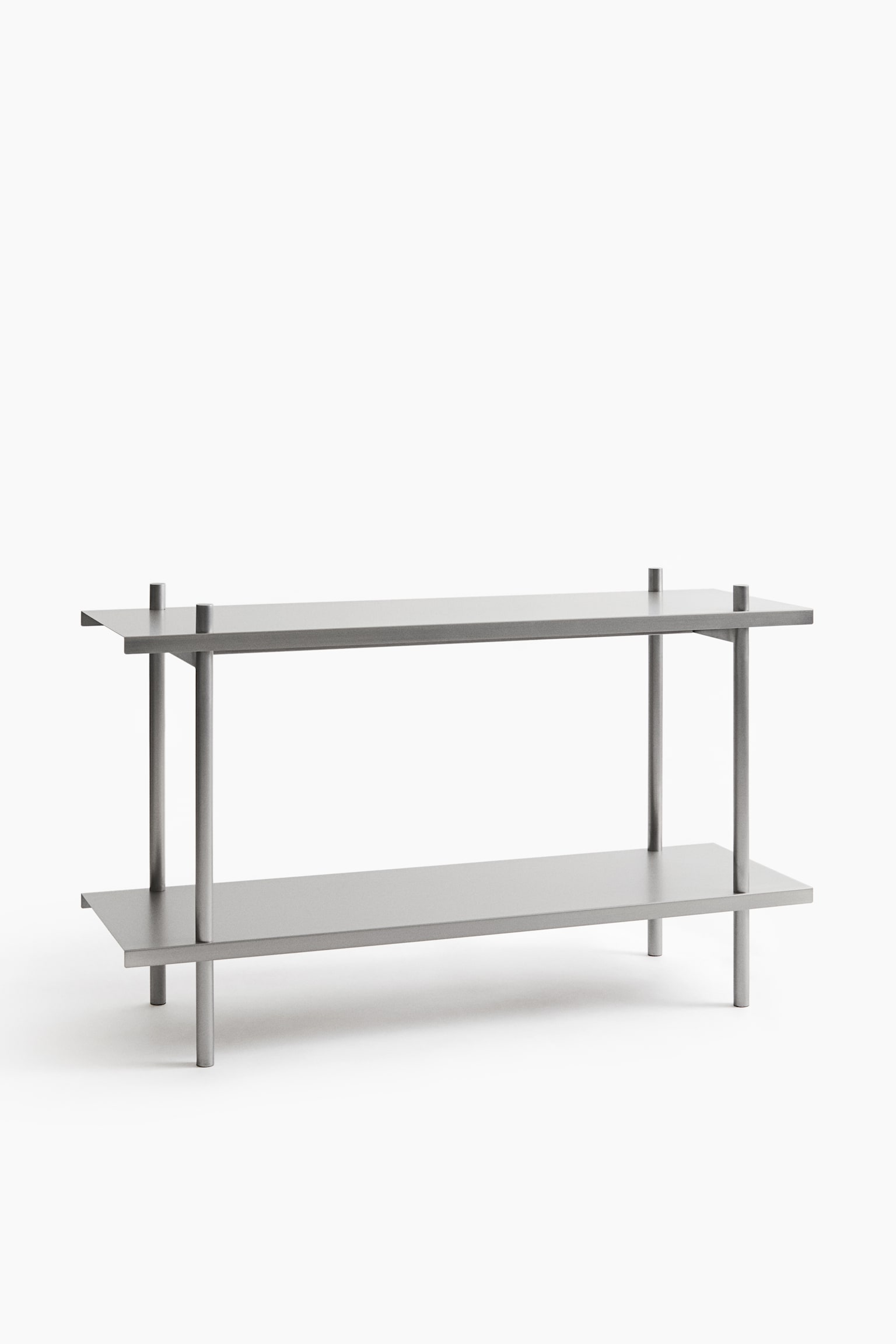 En tvÃ¥vÃ¥nings metallhylla Ã¤r vÃ¤nd framÃ¥t och har tvÃ¥ plana, rektangulÃ¤ra hyllplan med en matt silverfinish. Hyllplanen bÃ¤rs upp av fyra cylindriska metallstolpar som lÃ¶per genom hÃ¶rnen pÃ¥ varje nivÃ¥ och fortsÃ¤tter nedÃ¥t fÃ¶r att bilda benen. - 1