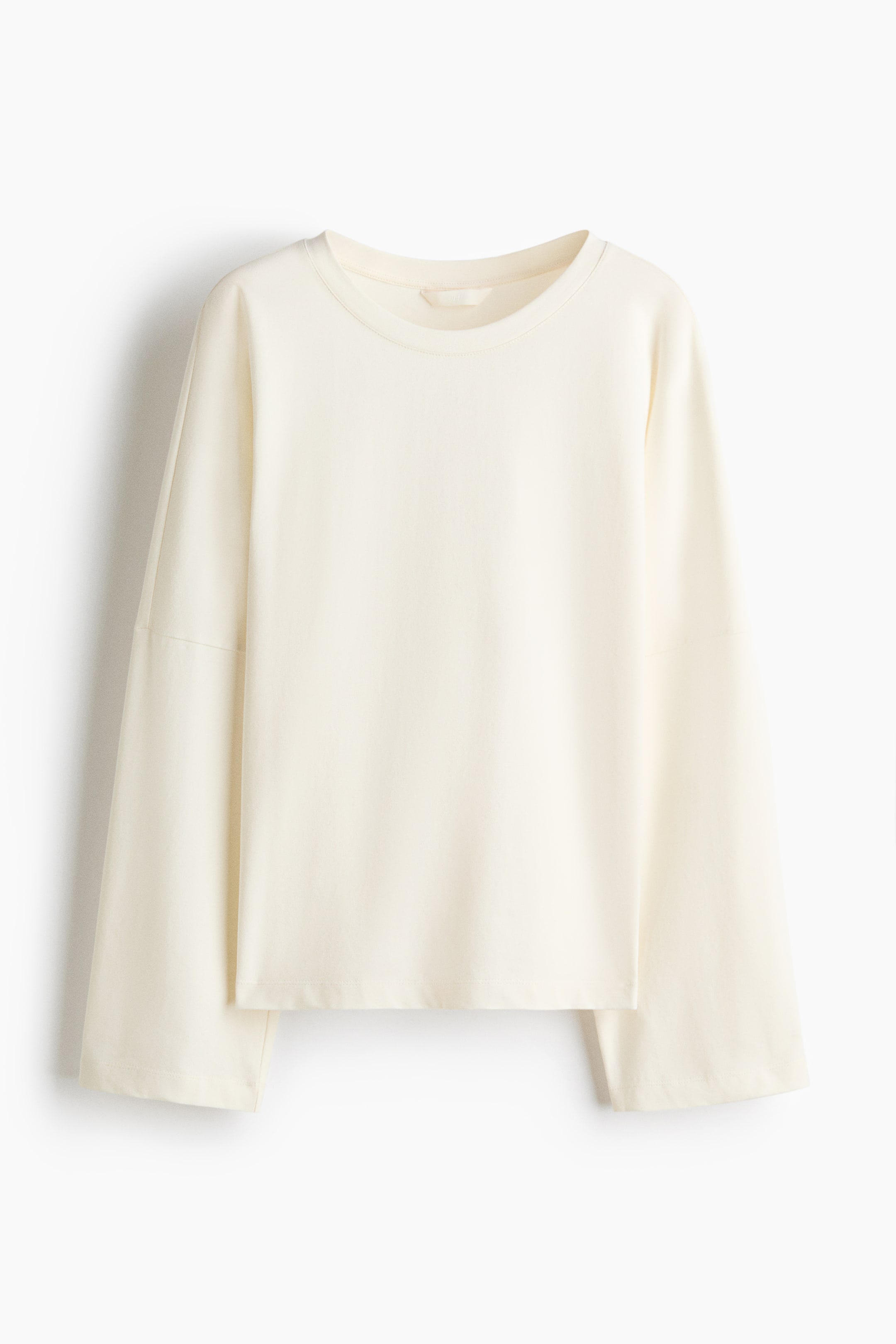 View larger image: A cream-colored top is shown from the front, featuring a round neckline and long sleeves. It has low dropped shoulders that contribute to a relaxed, slouchy effect.