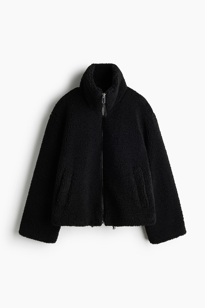 A black sherpa fleece jacket is facing front, showcasing a textured, fuzzy exterior, a high stand-up collar, and a full-length front zip closure. The jacket is featuring long, wide sleeves, subtle side welt pockets, and adjustable drawcords at the hem. - 1