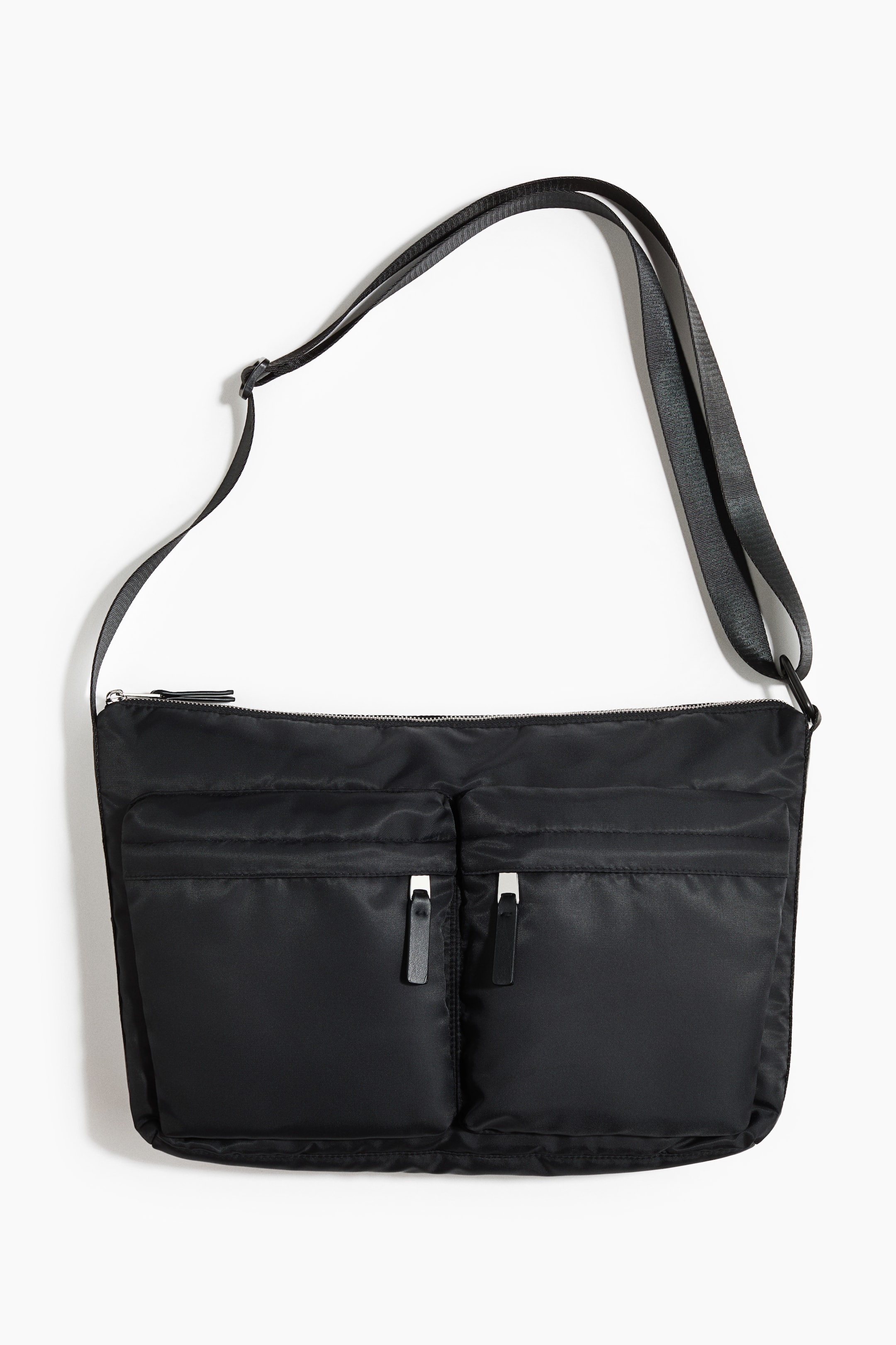 View larger image: A black crossbody bag is shown FRONT, featuring a main top zipper and two large front pockets. Each front pocket is secured with a silver zipper and a black pull tab, and a wide black strap is attached to the bag's top corners.