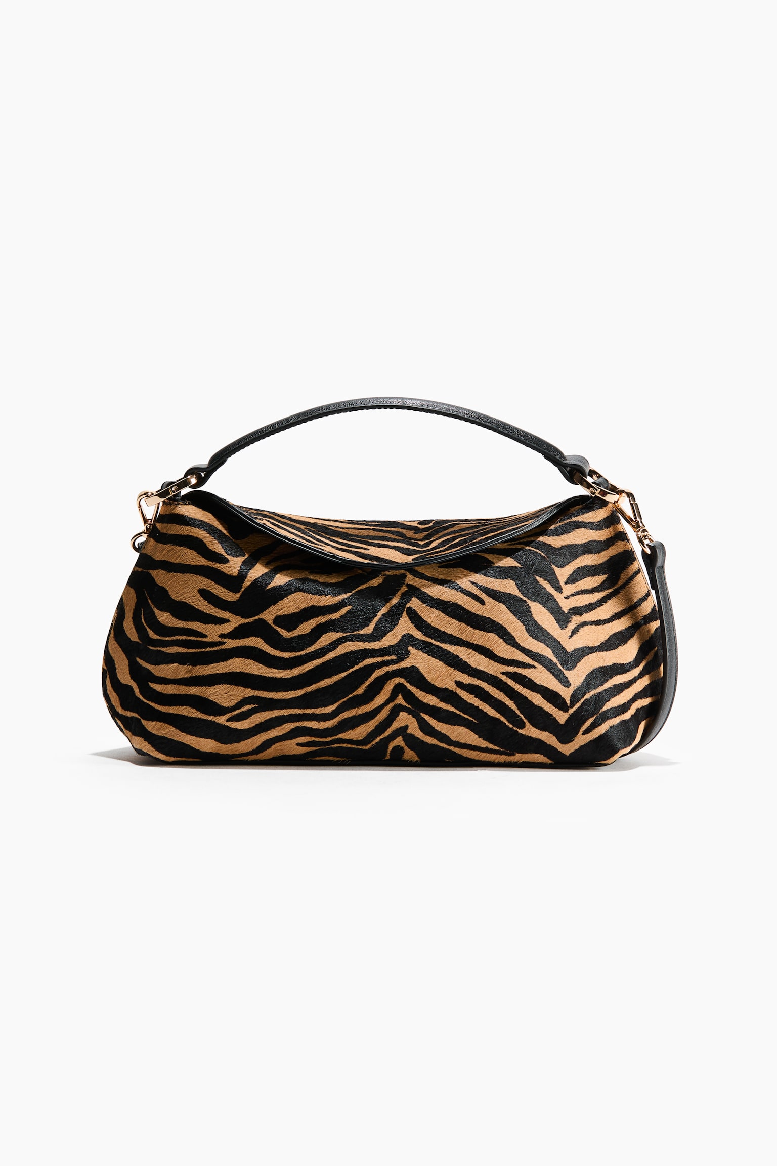 A tiger-print shoulder bag is shown from the front, showcasing a slouchy silhouette in a textured calf-hair finish with black and tan stripes. The bag features a curved black leather top handle secured by gold-tone metal hardware and matching black leather trim along the top flap.