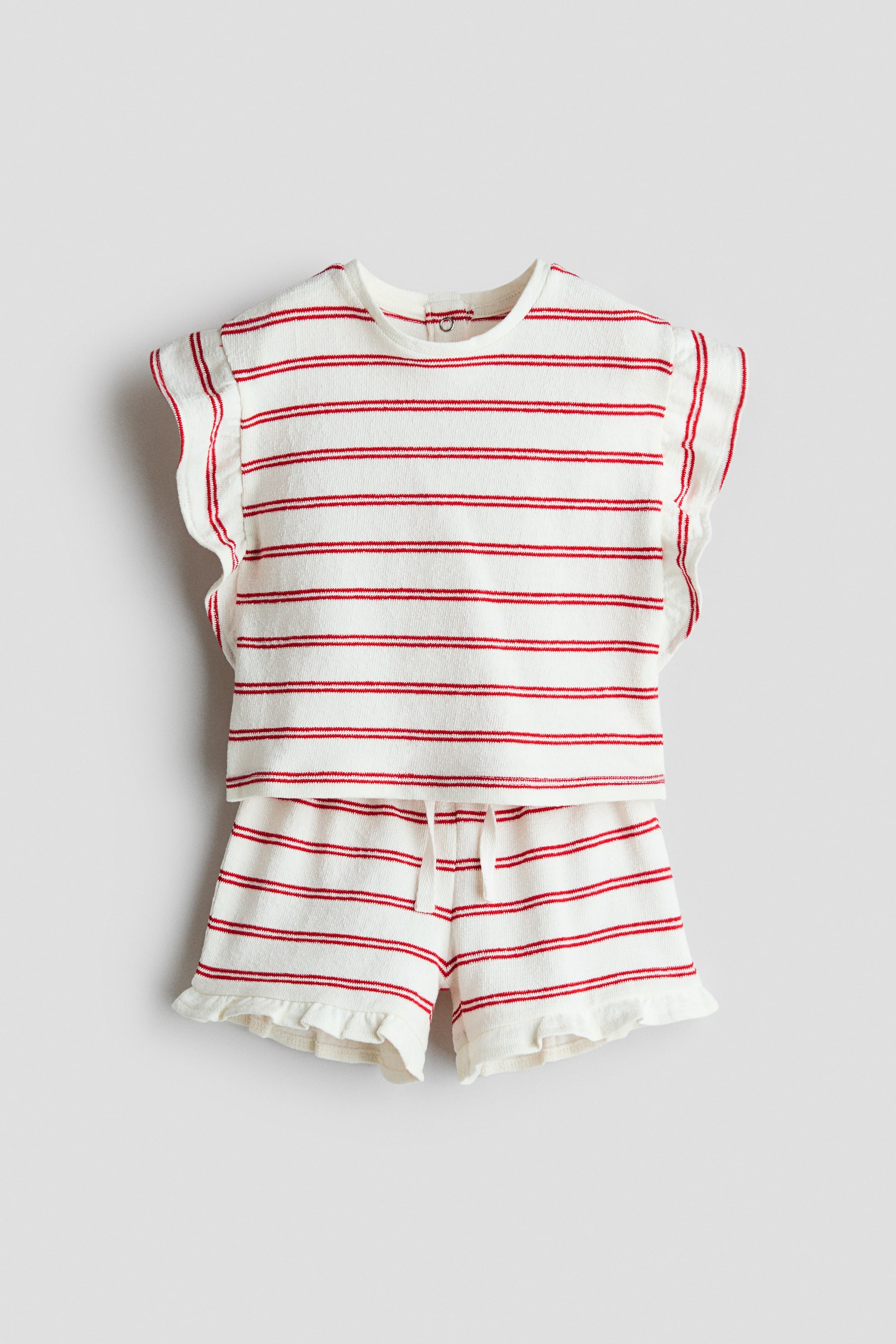 View larger image: "A white two-piece set with red horizontal stripes showcases a short-sleeved top and matching shorts. The textured knit top features a round neckline and ruffled sleeves, while the shorts are designed with a drawstring waist and ruffled hems."