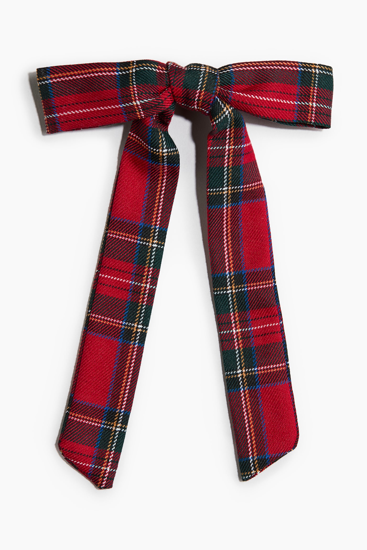A red tartan plaid bow is shown from the front, featuring a classic pattern of red, green, white and yellow stripes. The bow displays a structured central knot with two long, wide fabric tails hanging down.