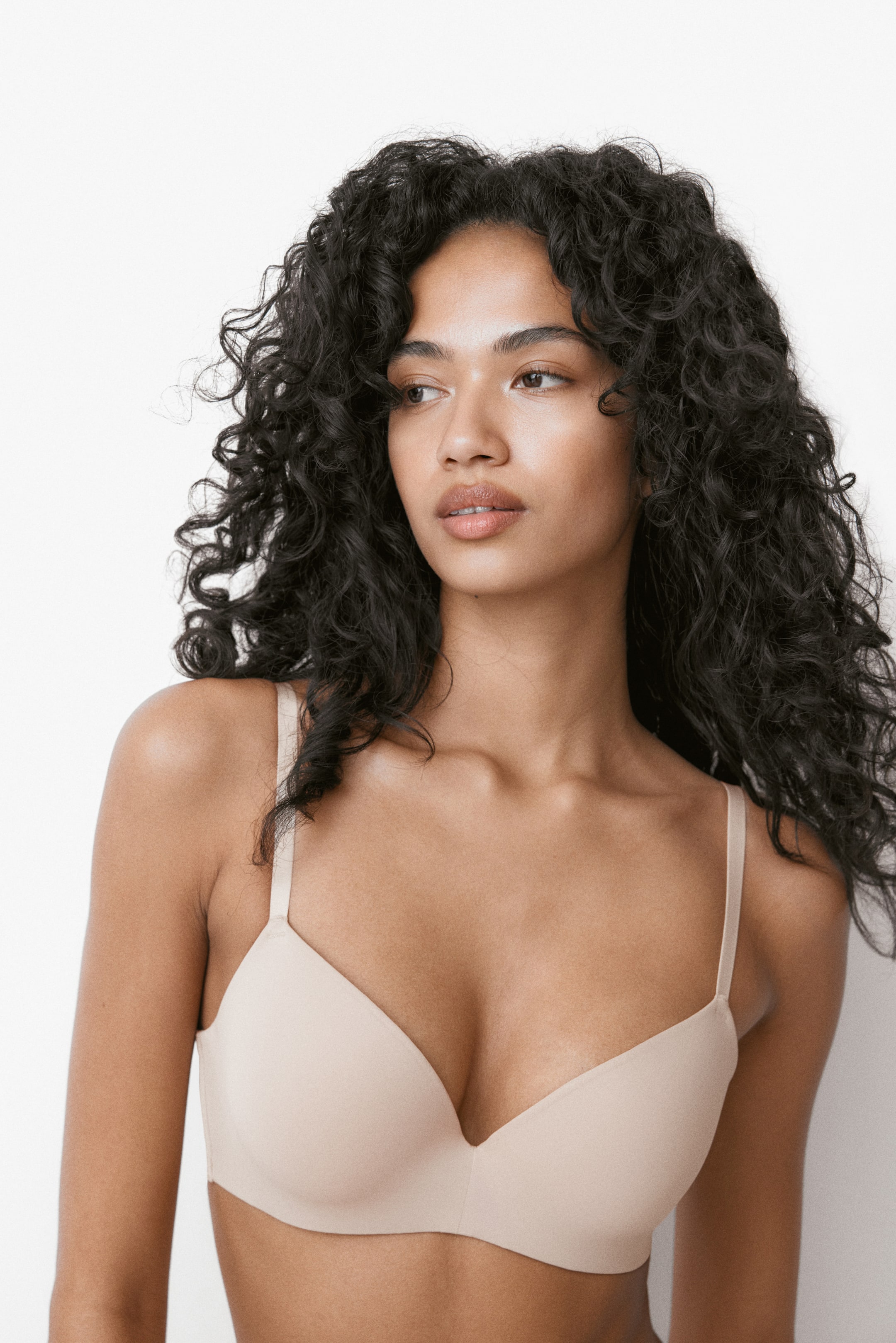 View larger image: A beige seamless bra is being worn, featuring smooth moulded cups creating a V-neckline and thin, adjustable straps.