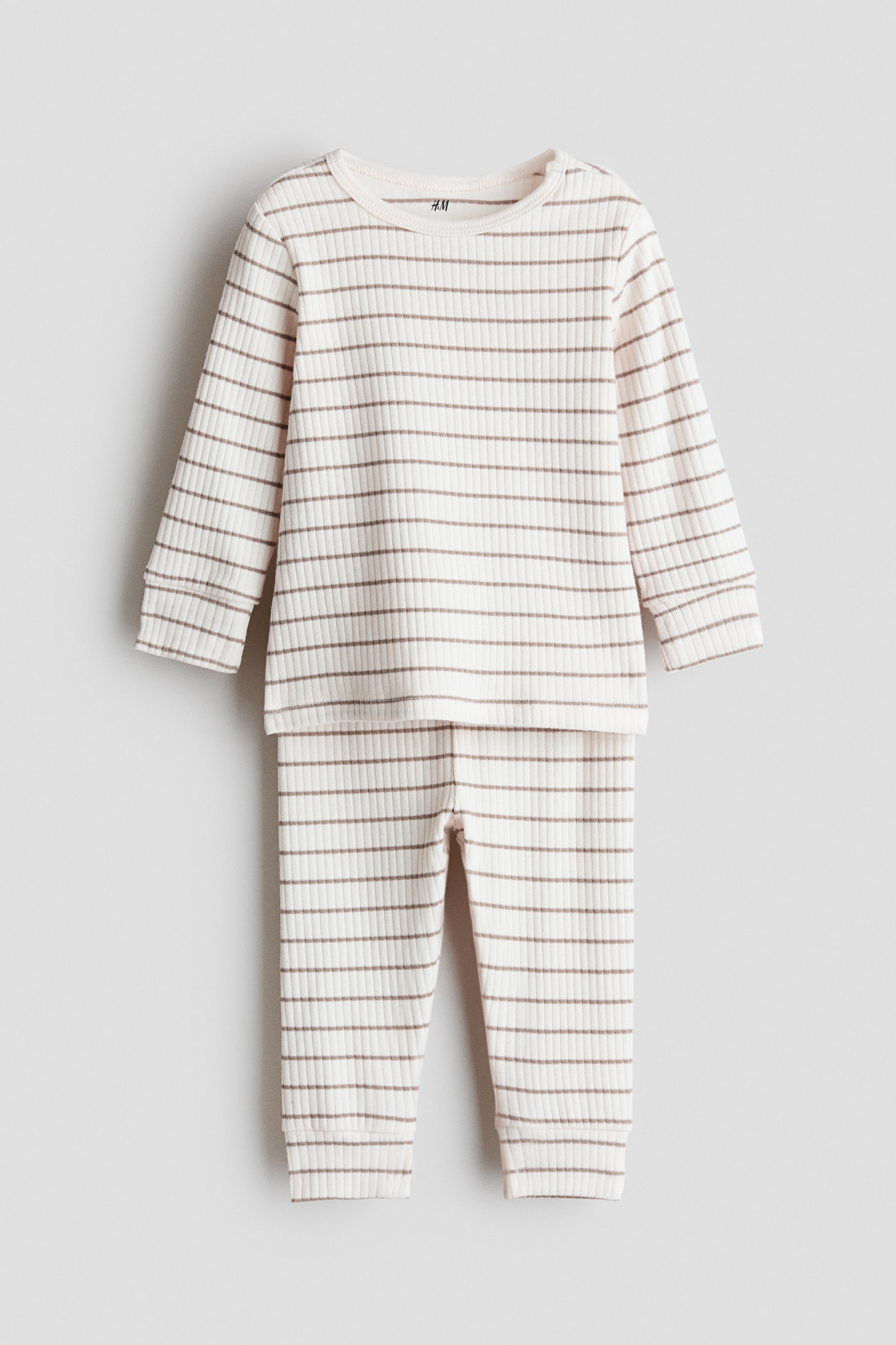 Visa större bild: Ribbad bomullssats, framifrån. Den långärmade toppen och de matchande byxorna är gjorda av benvit ribbad bomull med horisontella bruna ränder. Toppen har en rund hals och ribbade muddar, och byxorna visar ribbade muddar vid anklarna.