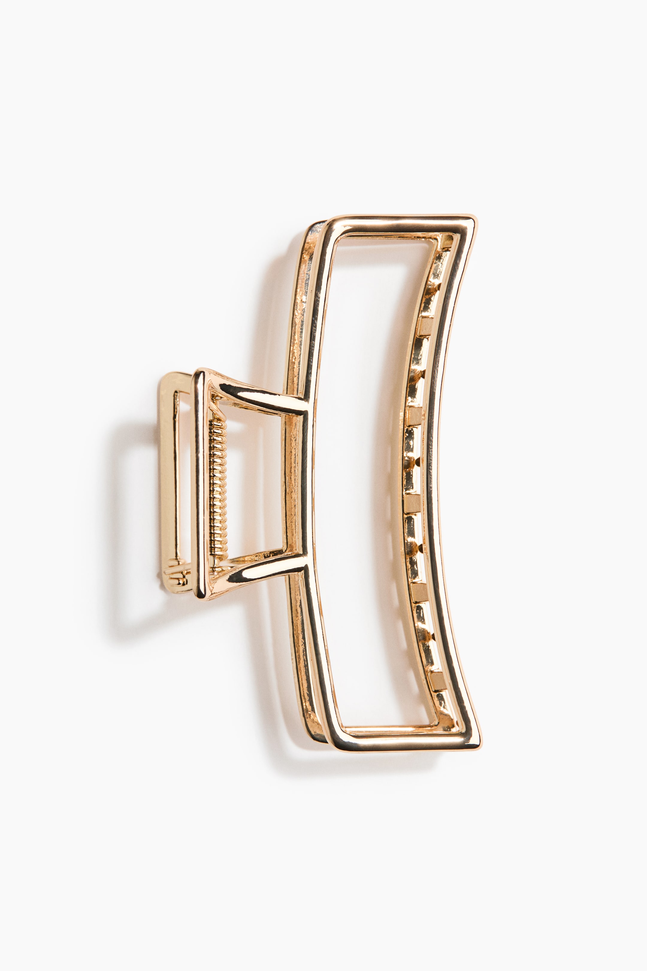 View larger image: A gold-toned metal hair claw clip is positioned with its jaws slightly open, featuring a large, curved rectangular frame and a smaller opposing jaw. A visible spring mechanism connects the jaws, whose inner edges are displaying small, square gripping teeth.
