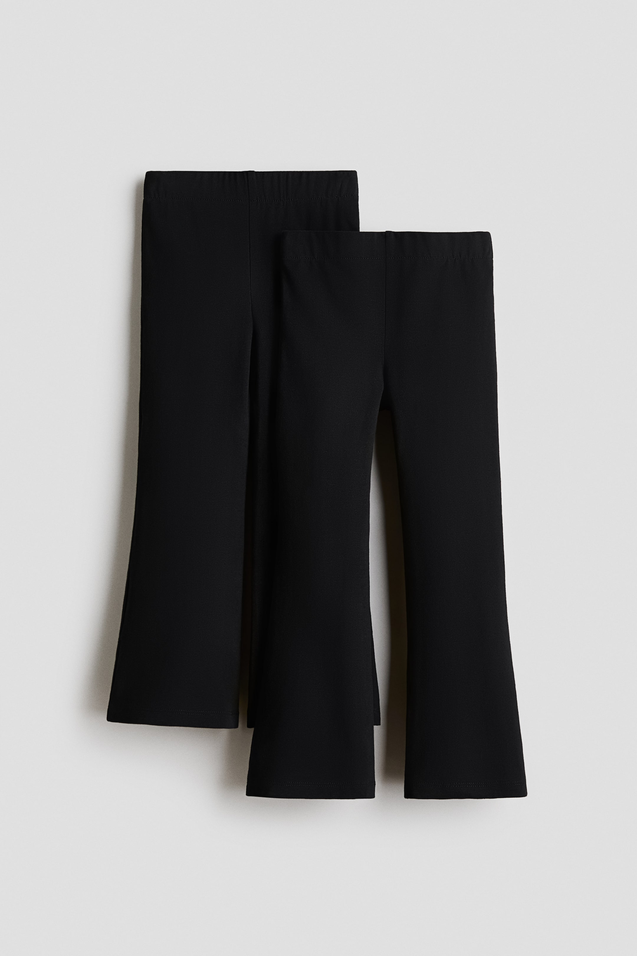 View larger image: Two pairs of black flared leggings are showcased from the front, highlighting their elasticated waistbands and sleek fabric. Designed with flared leg openings, one pair is slightly set behind the other.