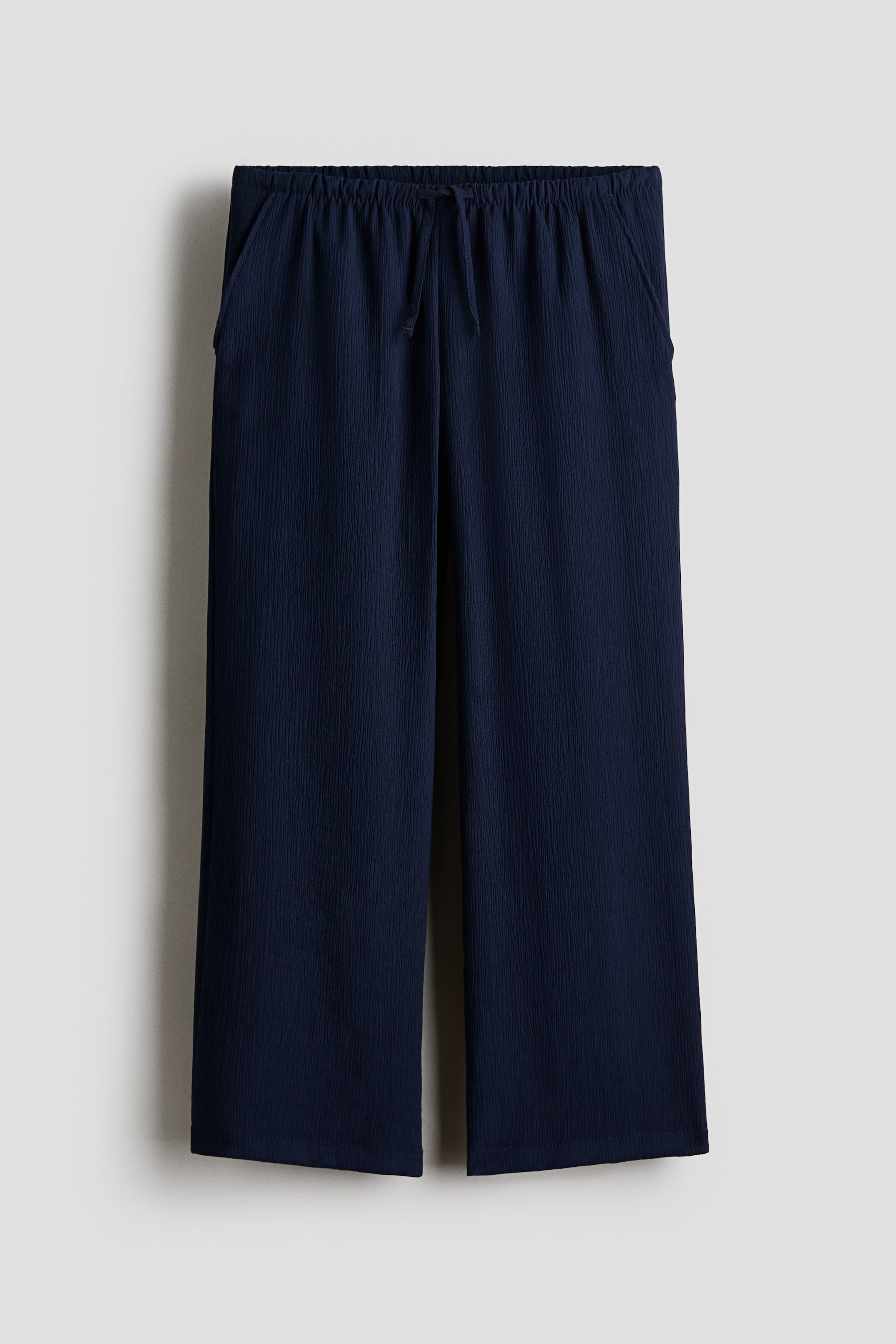 View larger image: Navy blue relaxed-fit trousers are featured from the front, highlighting an elasticated drawstring waist, diagonal side pockets, and a subtly textured woven fabric.