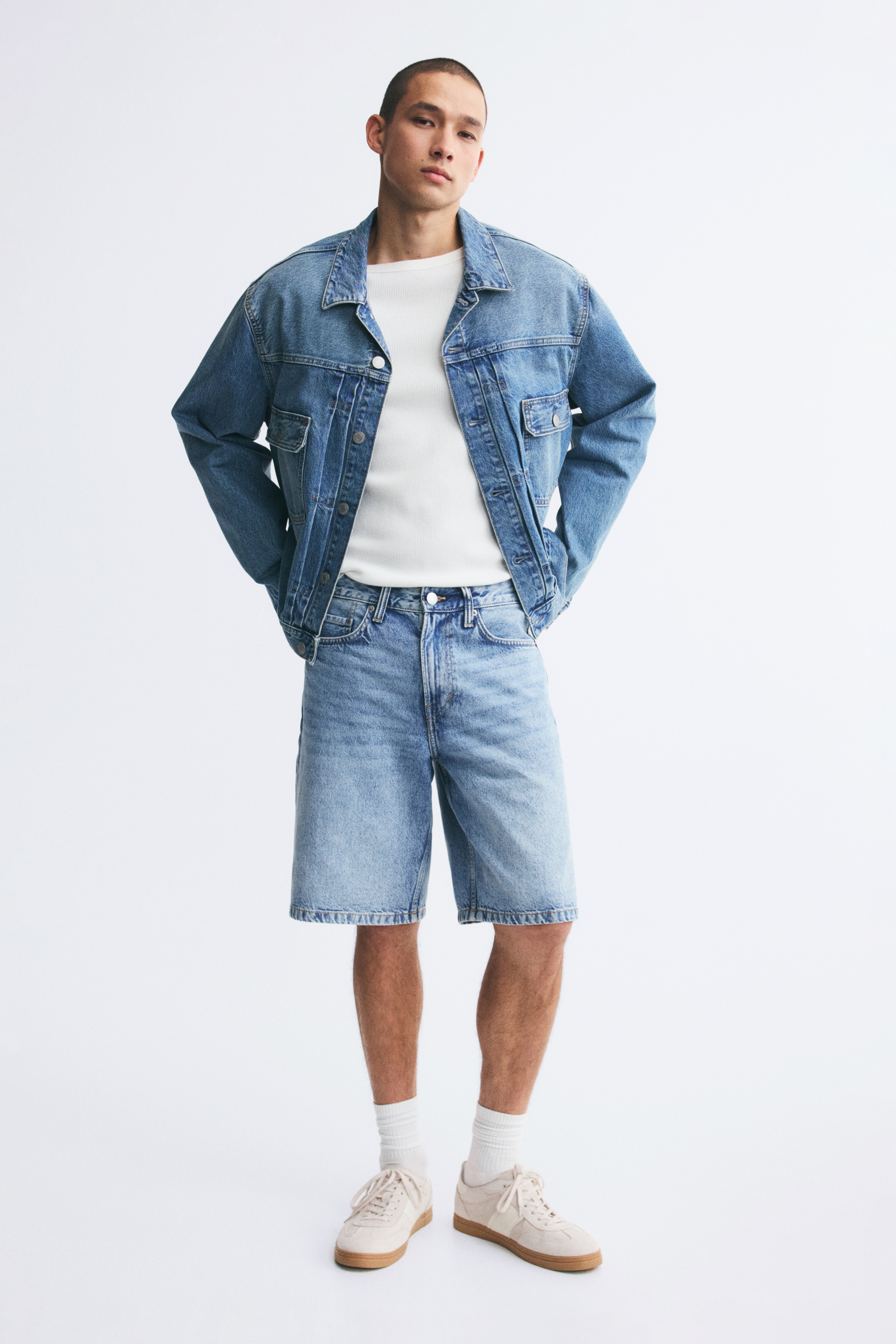 I pantaloncini di jeans azzurri vengono presentati dalla parte anteriore. Presentano un lavaggio scolorito, una chiusura con bottone e zip e tre tasche frontali visibili. Le gambe larghe cadono sopra il ginocchio.