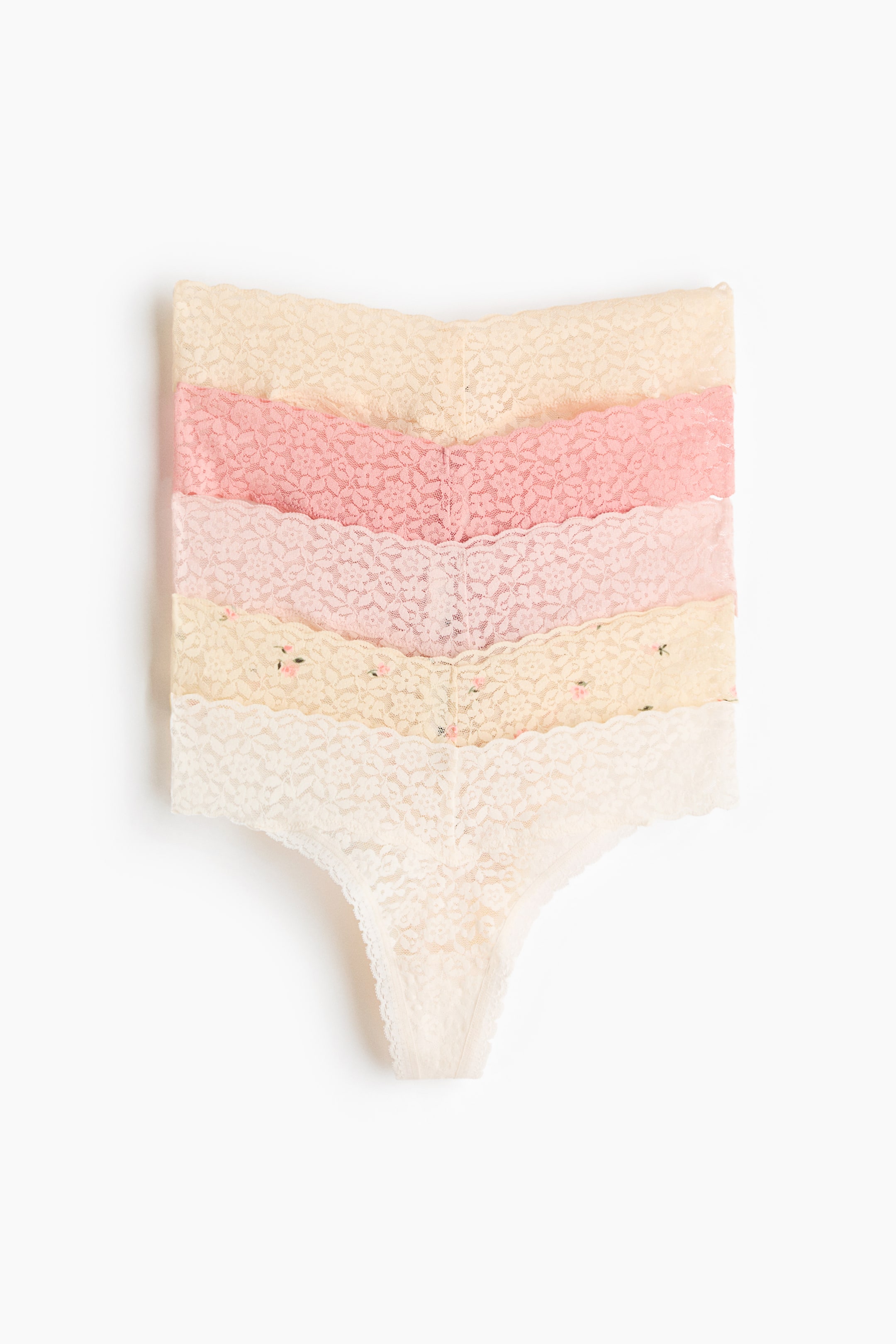 View larger image: Five lace thongs are neatly stacked, facing front. They showcase delicate floral lace patterns in hues of cream, light pink, and peach. One cream thong displays small scattered flower details, with each thong highlighting scalloped edges along its waistband.