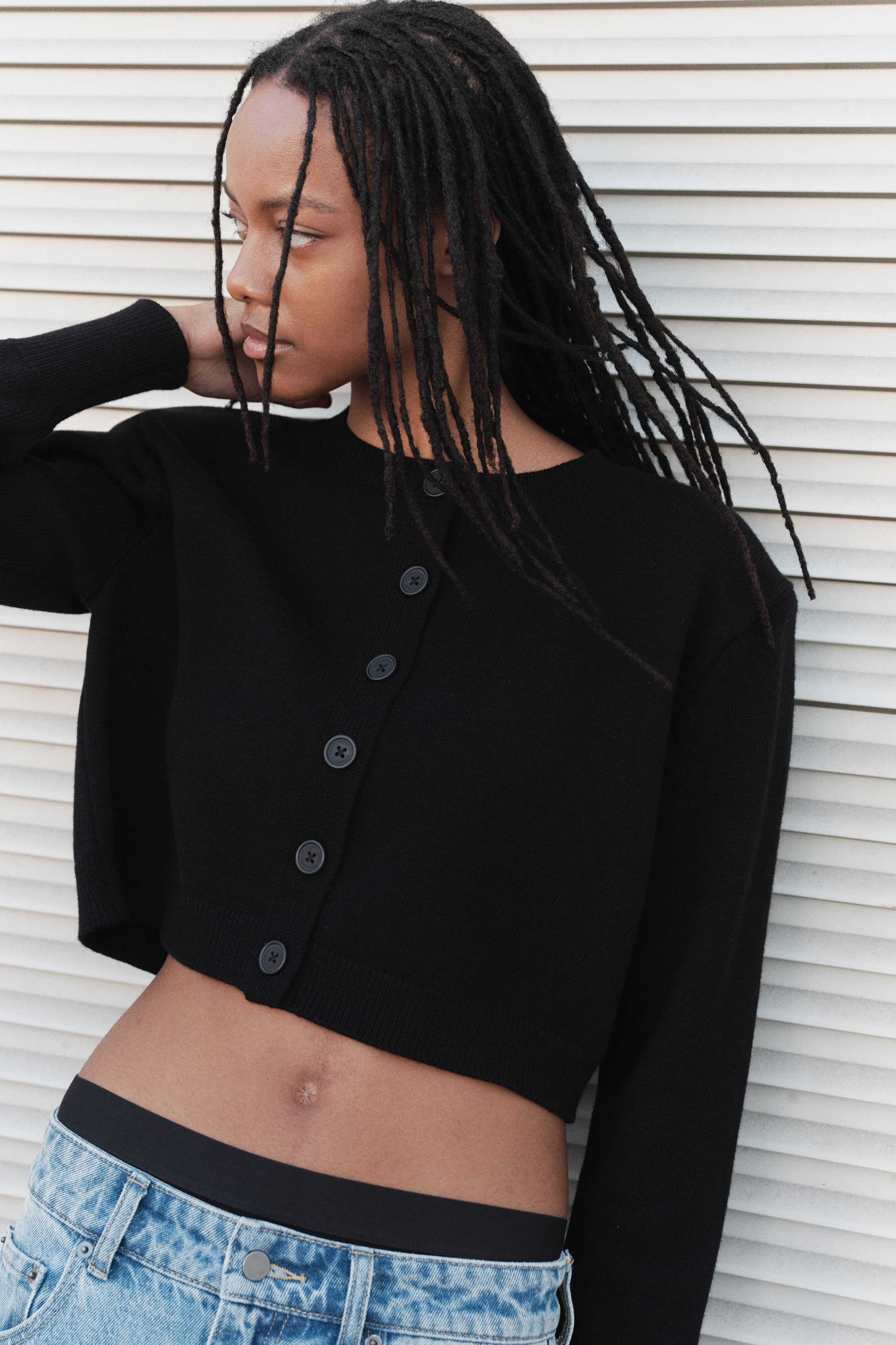 Visualizza l'immagine ingrandita: Un cardigan corto in maglia nero è mostrato frontalmente, con scollo rotondo e chiusura frontale con bottoni scuri. È caratterizzato da maniche lunghe e dettagli a coste lungo lo scollo, la patta con bottoni, i polsini e l’orlo.