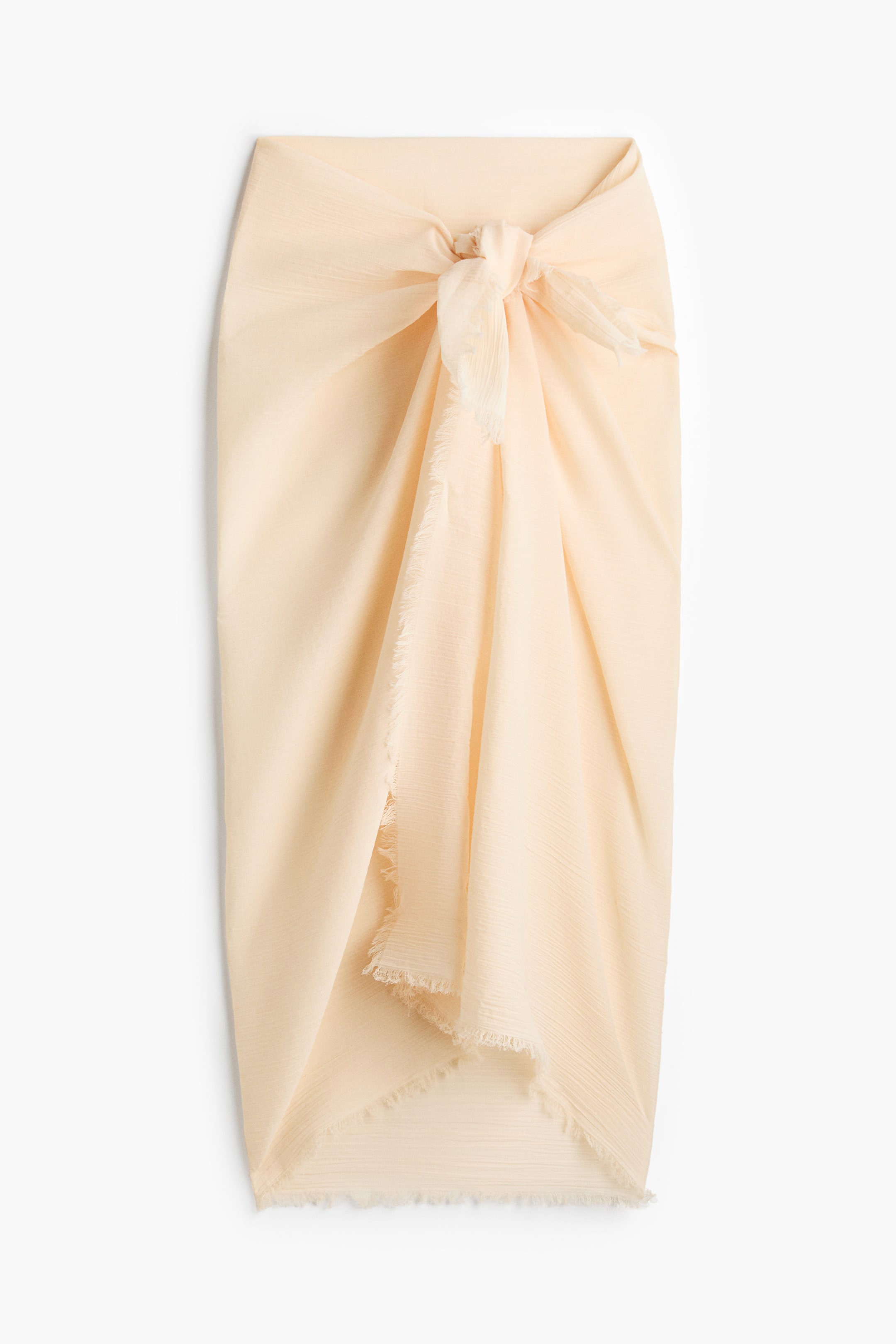 View larger image: A light beige crinkled sarong features a central knot at the top, from which the fabric elegantly drapes downwards. It showcases frayed edges along the bottom and at the tied fabric ends.