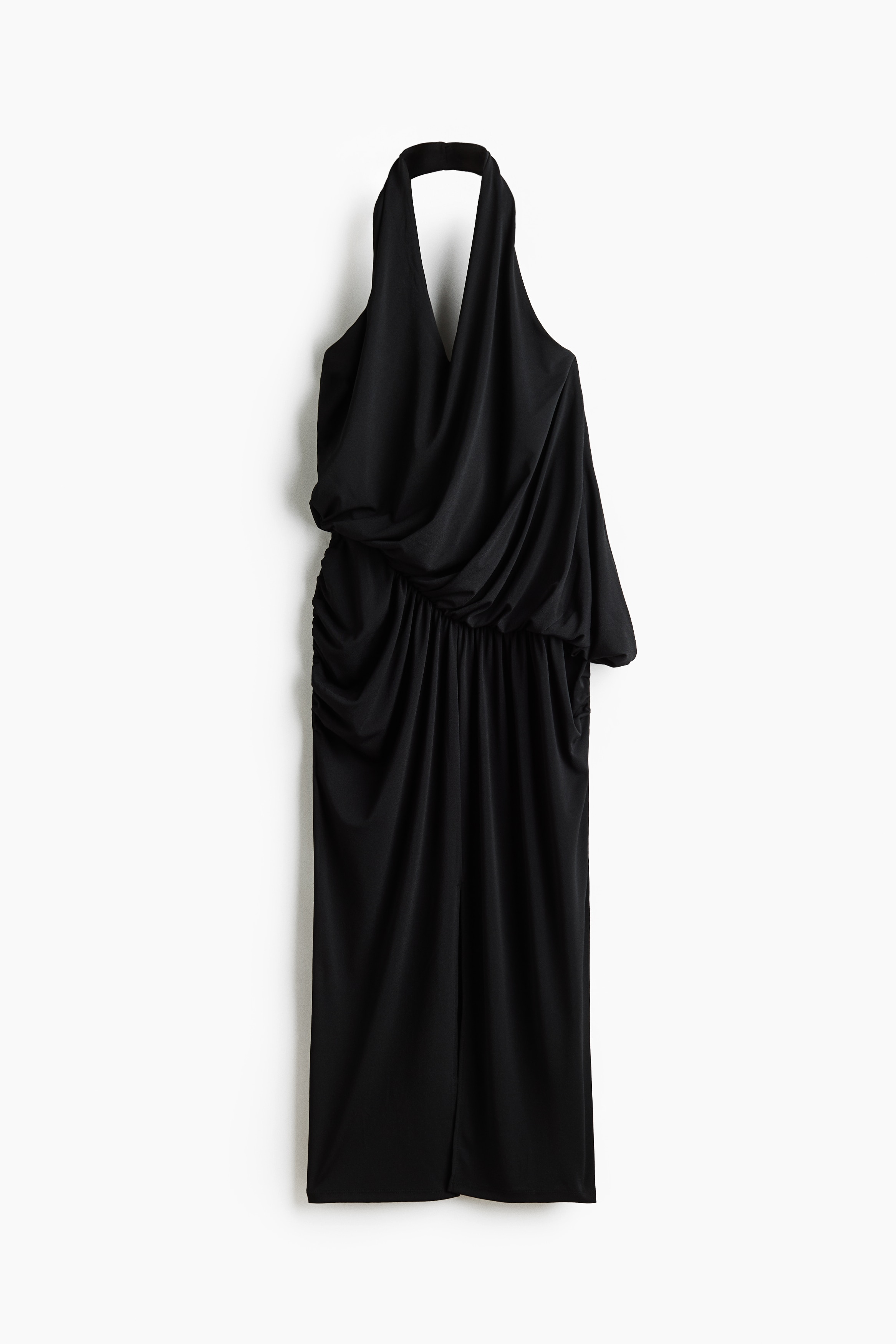 A black draped halterneck dress is being worn by the model, featuring a deep V-neck, draped fabric detailing at the waist, and a midi skirt with a high front slit. The dress is styled with black leather knee-high boots.