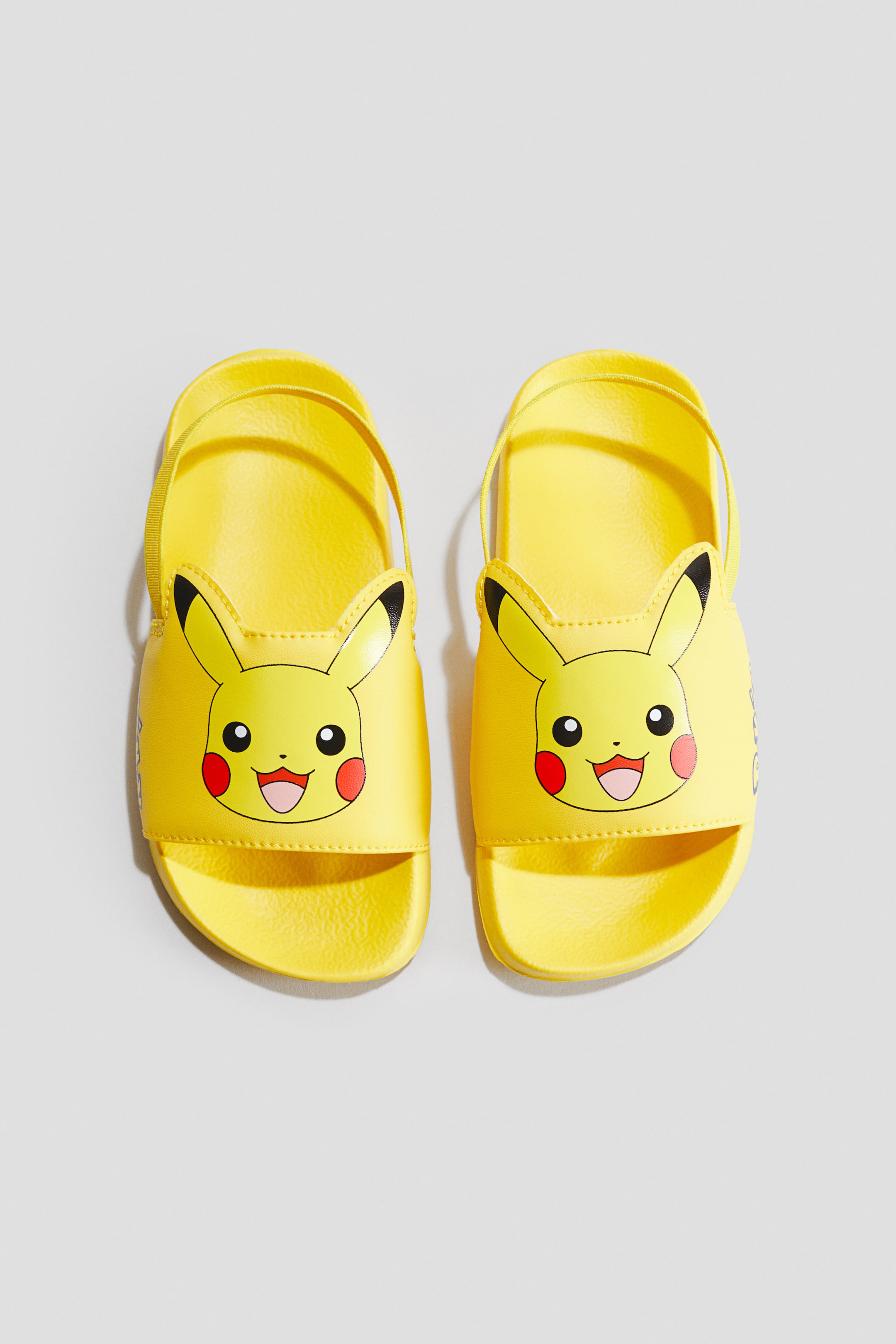 הצגת תמונה גדולה יותר: זוג נעלי בריכה צהובות עם הדפס של פיקאצ'ו על הרצועה הרחבה של כף הרגל, כולל אוזניים עם קצוות שחורים המתרוממות כלפי מעלה. כל נעל כוללת גם רצועת עקב דקה וסוליה מעוצבת, נצפית מהחזית.
