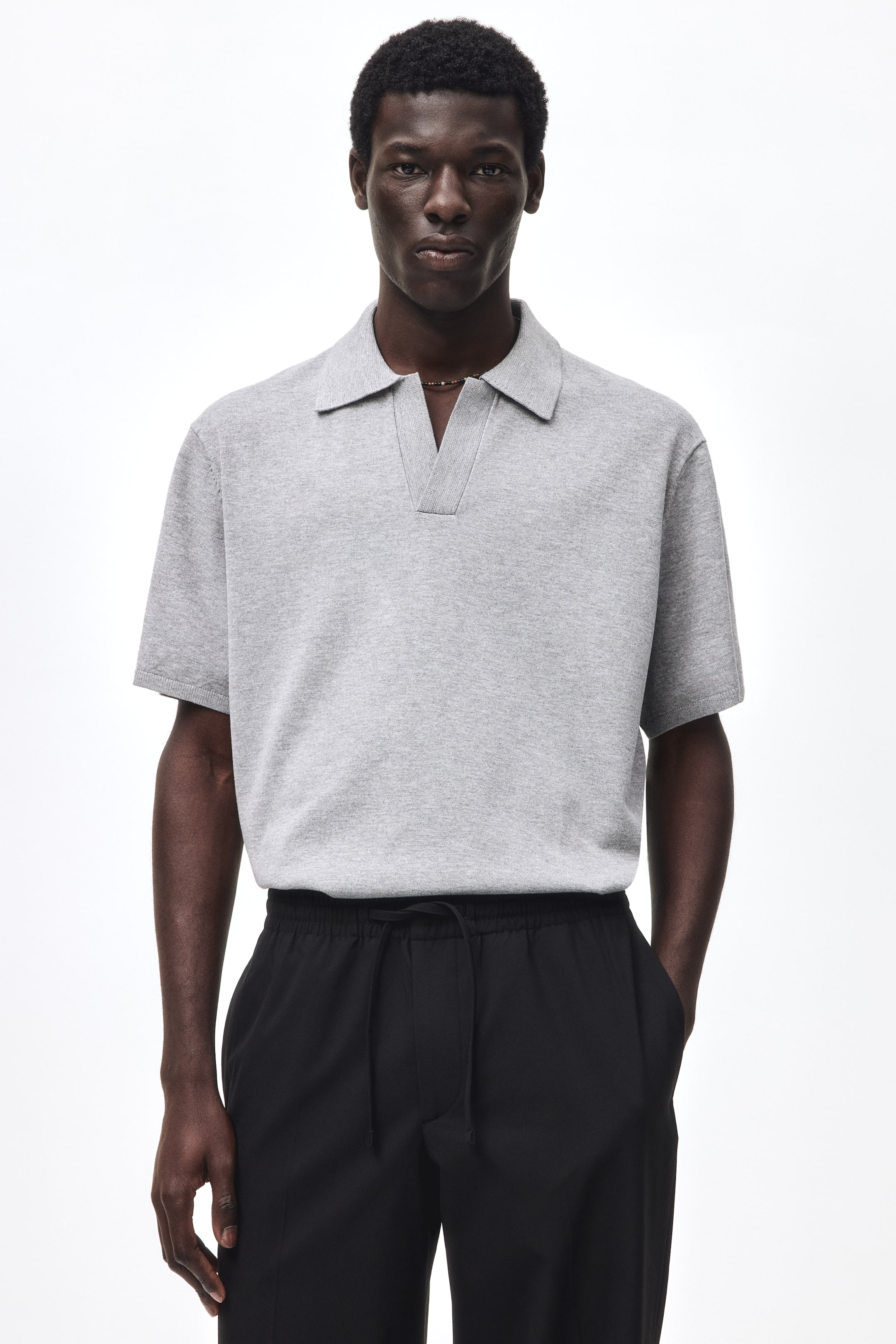 View larger image: The model is wearing a light gray knit polo shirt featuring short sleeves, a collar, a V-shaped opening, and ribbed cuffs and hem.