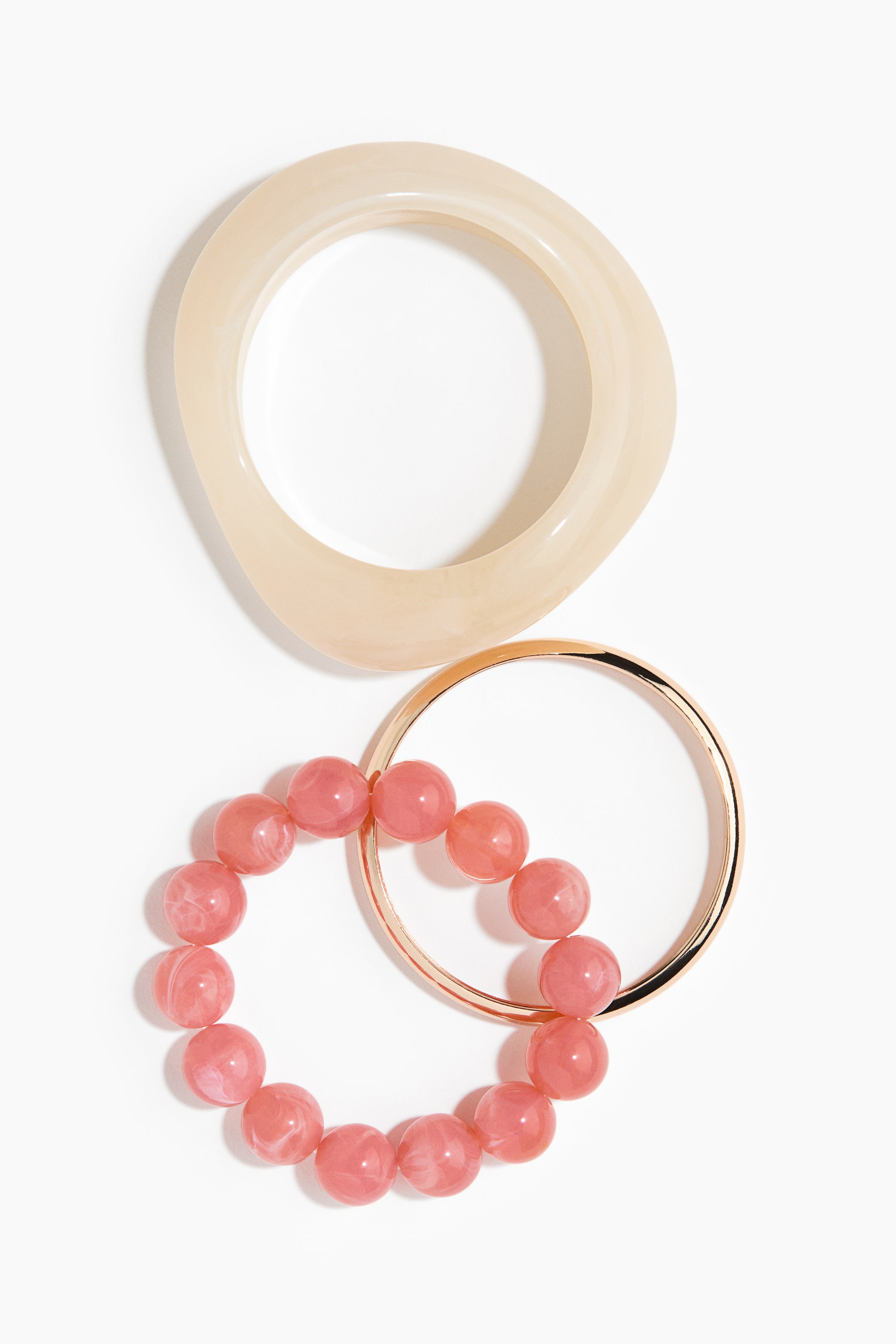View larger image: A set of three bracelets is shown, featuring an irregular oval-shaped milky-beige bangle, a thin gold-tone metal bangle, and a pink marbled beaded stretch bracelet.