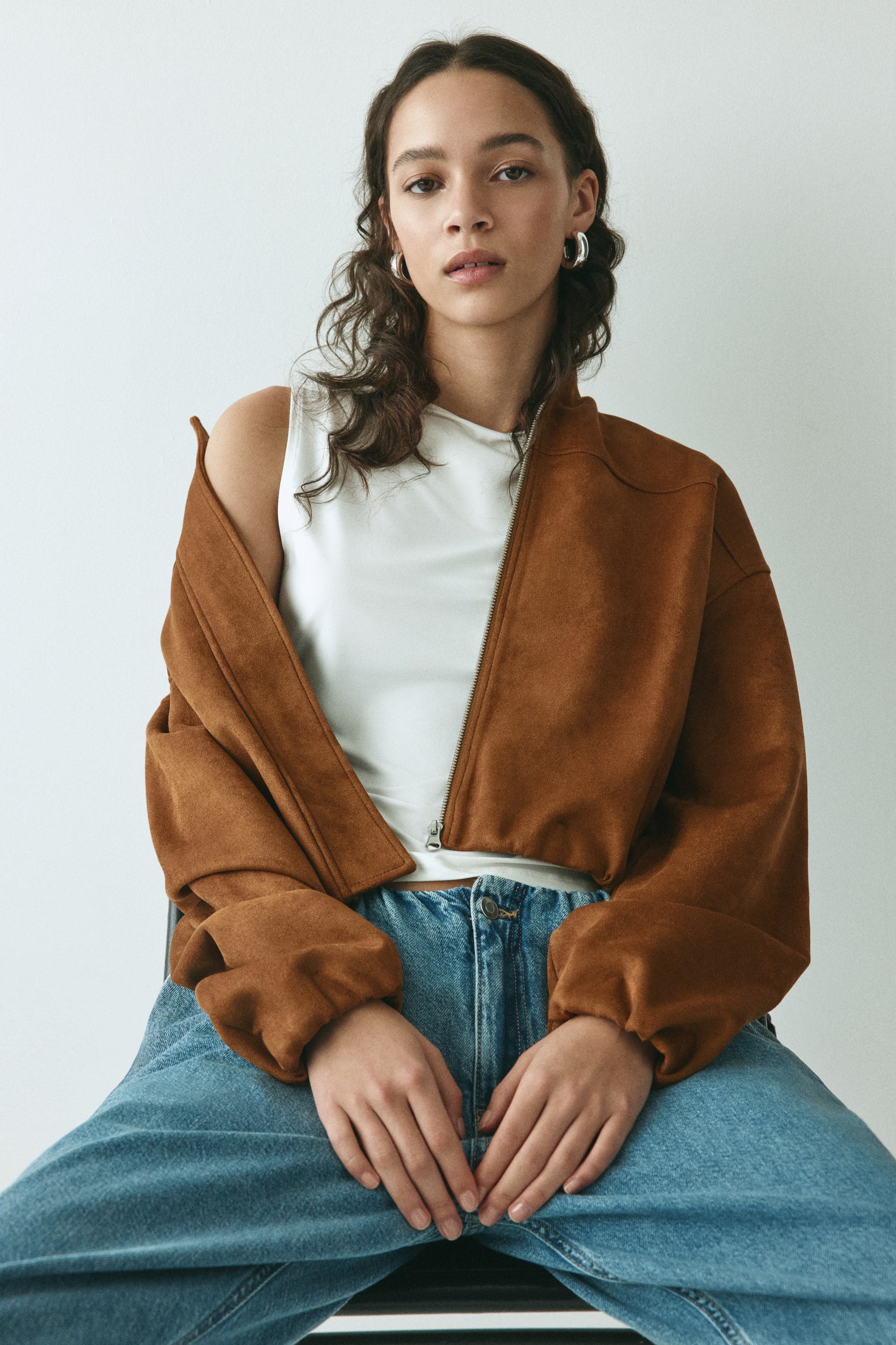 Visualizza immagine più grande: La modella indossa una giacca oversize in heavy jersey con una finitura morbida e felpata. Presenta una zip frontale parzialmente aperta, spalle scese ed elastico coperto ai polsini e all'orlo, che lascia intravedere un top bianco sottostante.