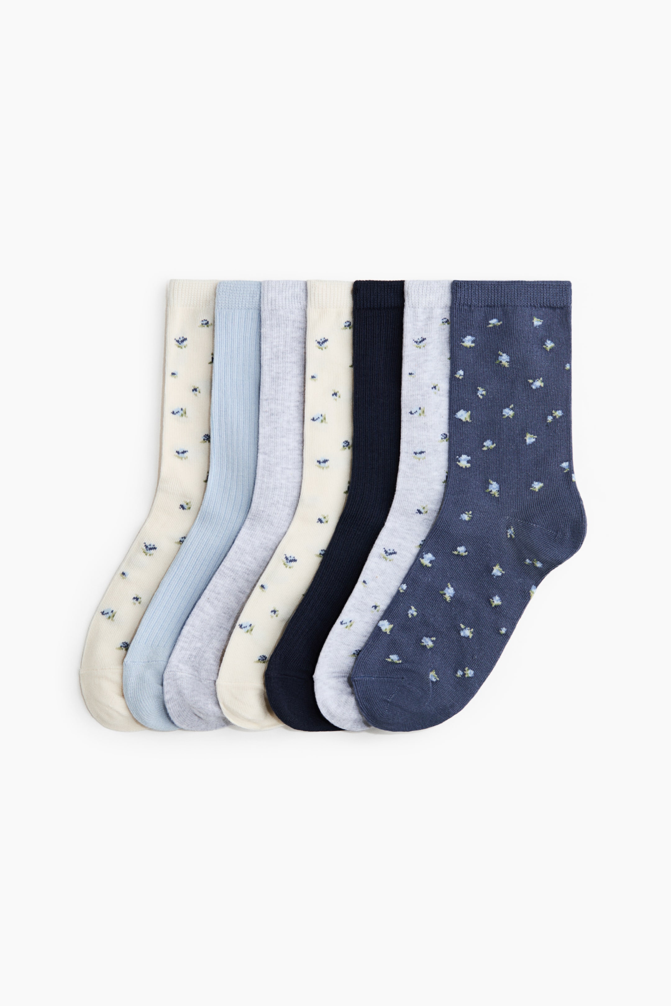 View larger image: Fine-knit socks in a soft cotton blend are presented as a set of seven individual socks, arranged in a fan from left to right, all featuring ribbed cuffs. They showcase a variety of designs, including solid light blue with a ribbed texture, solid light gray, and solid dark blue, alongside socks featuring a small blue floral print on cream, light gray, and dark blue backgrounds.