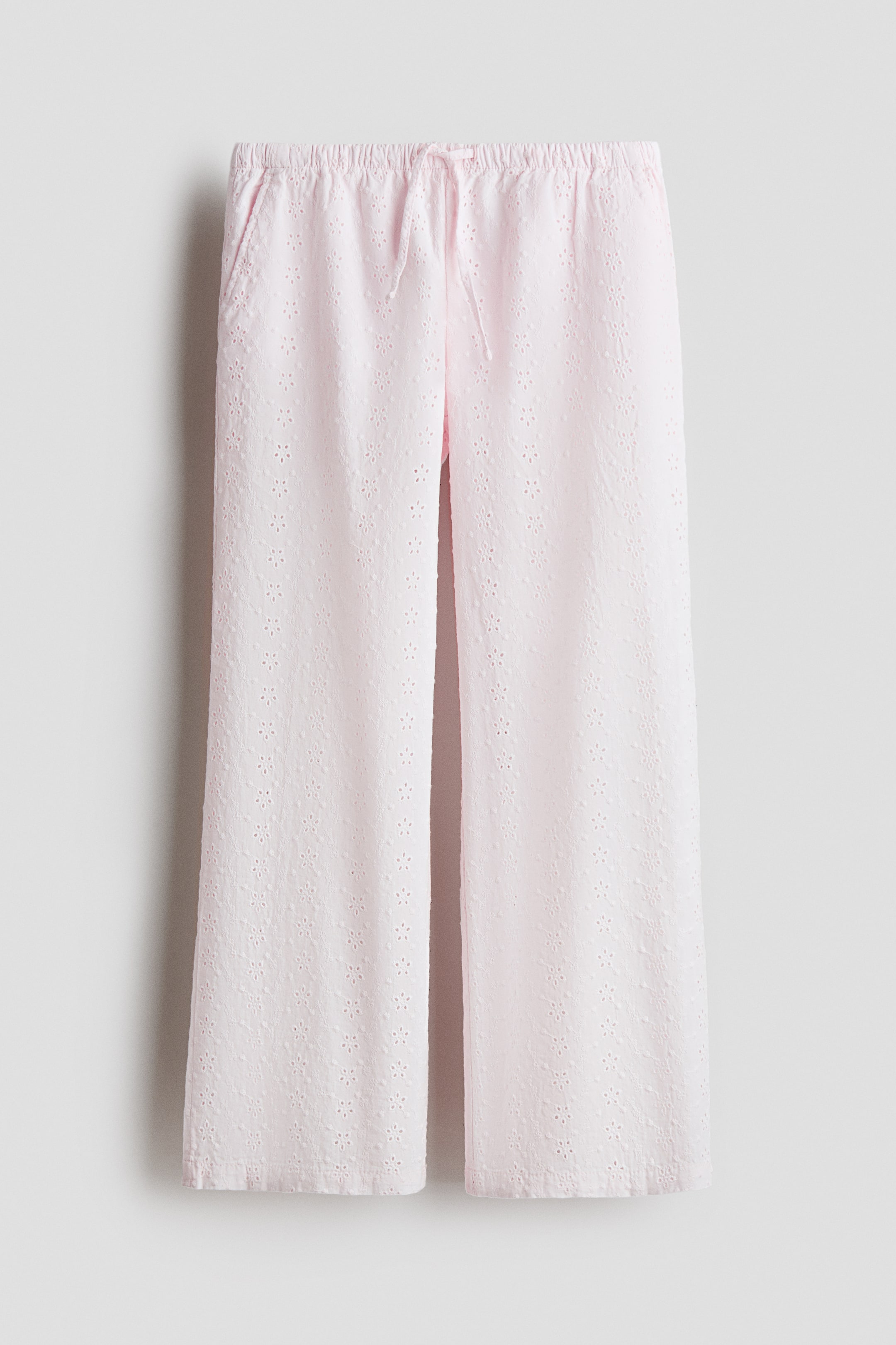 View larger image: Light pink wide-leg pants feature an all-over eyelet pattern on the fabric. The front showcases an elasticized drawstring waistband and side seam pockets.
