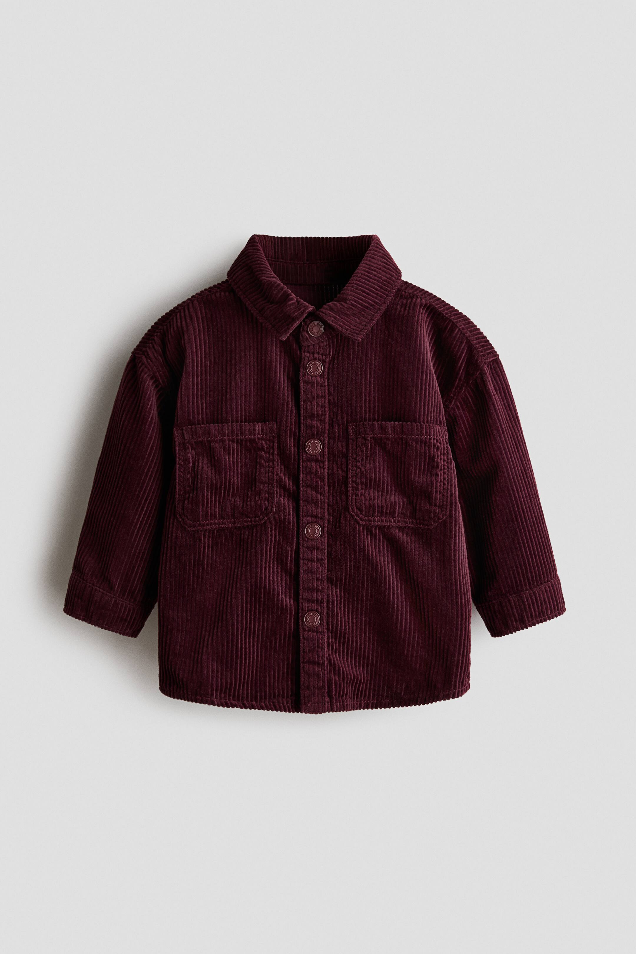 View larger image: A burgundy corduroy shirt is shown from the front, featuring a turn-down collar, press-stud fasteners along the front placket, and two open chest pockets. The shirt highlights a ribbed fabric texture, long sleeves with cuffs, and a slightly rounded hem.