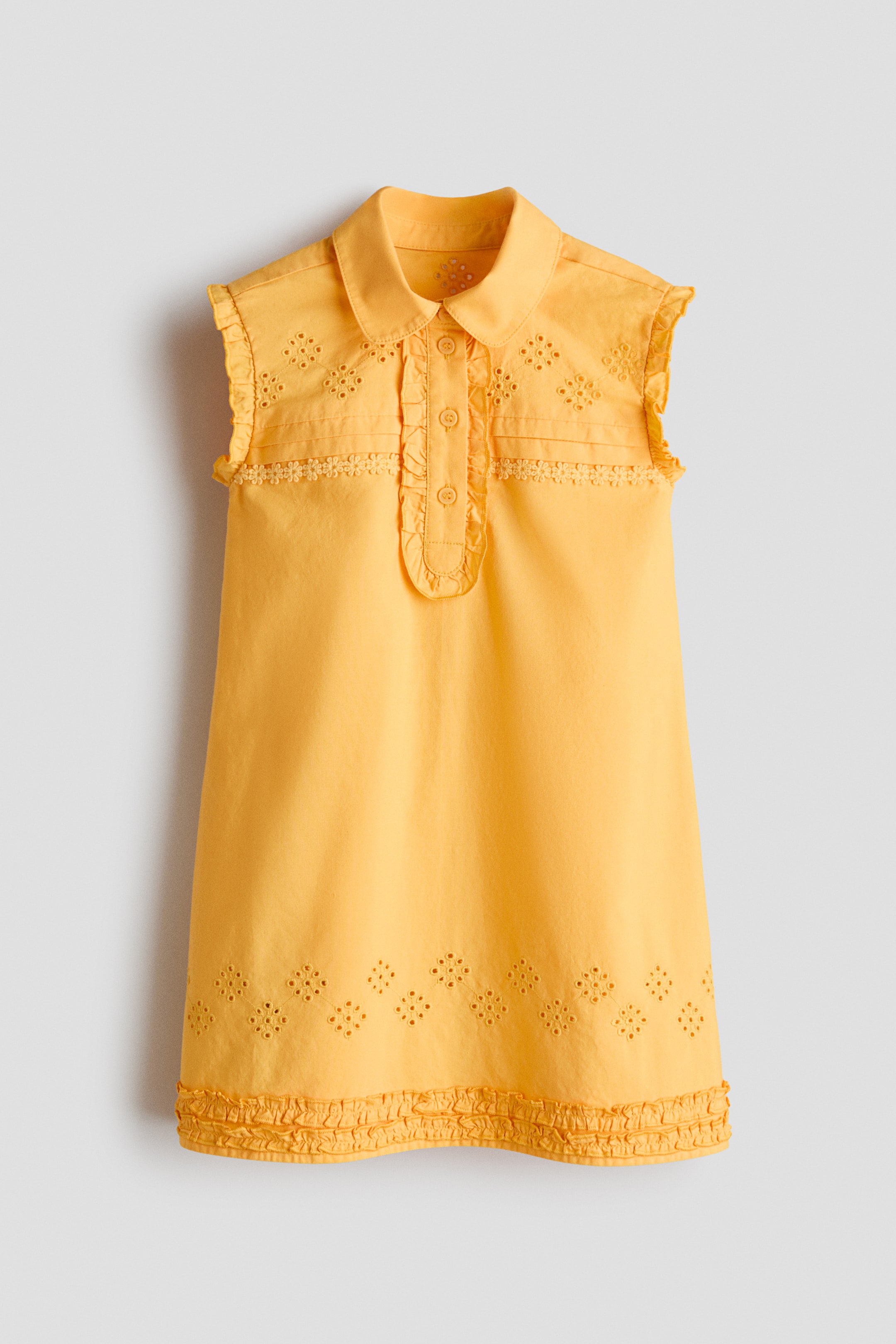 View larger image: A yellow sleeveless dress is showcasing its front, adorned with a pointed collar, ruffled armholes, and a ruffled button placket. Eyelet embroidery embellishes the upper bodice panels and the lower skirt section, above a ruffled hem.