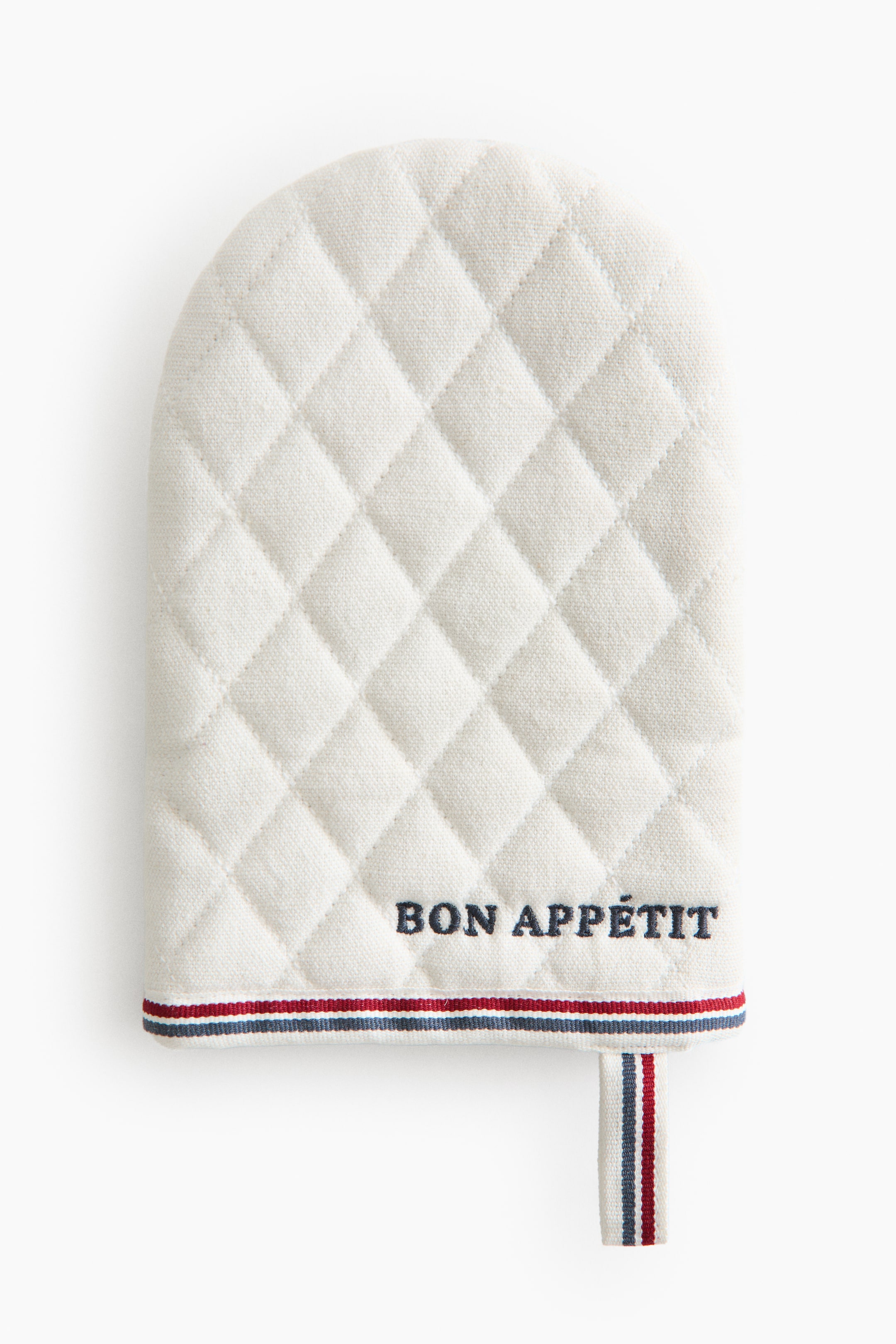 View larger image: The cream-coloured oven mitt features a diamond quilted pattern across its front surface. Dark blue embroidery spelling "BON APPÉTIT" is displayed above a red, white, and blue striped trim at the bottom, with a matching hanging loop extending from the right.