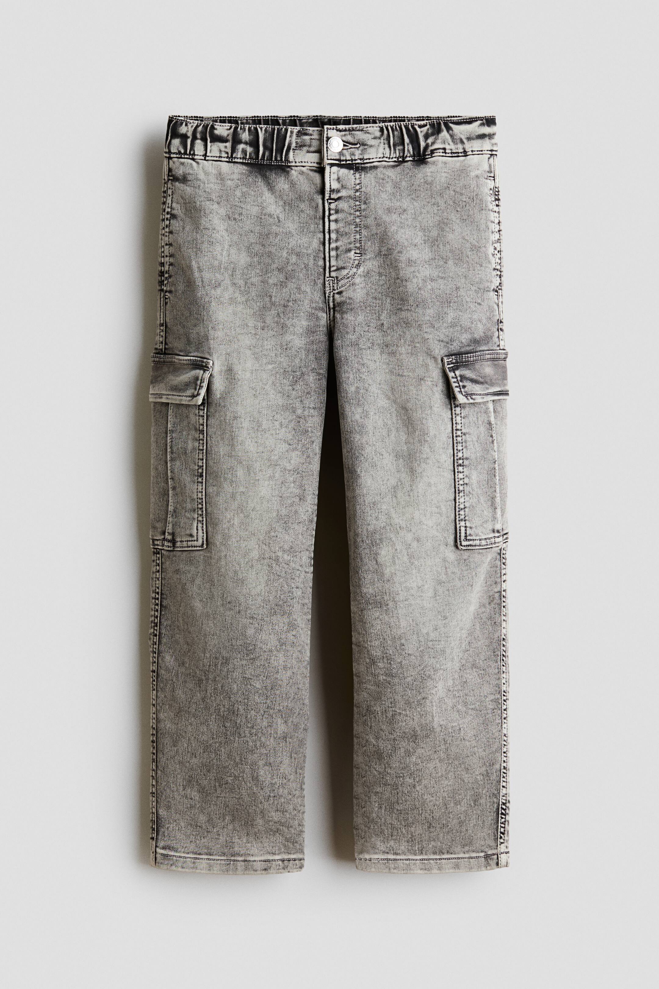 View larger image: A pair of grey acid-wash denim cargo trousers is shown from the front, featuring a straight-leg silhouette and a gathered elasticated waistband with a single-button fastening. The trousers display flap cargo pockets on both sides of the thighs with prominent topstitching along the seams.