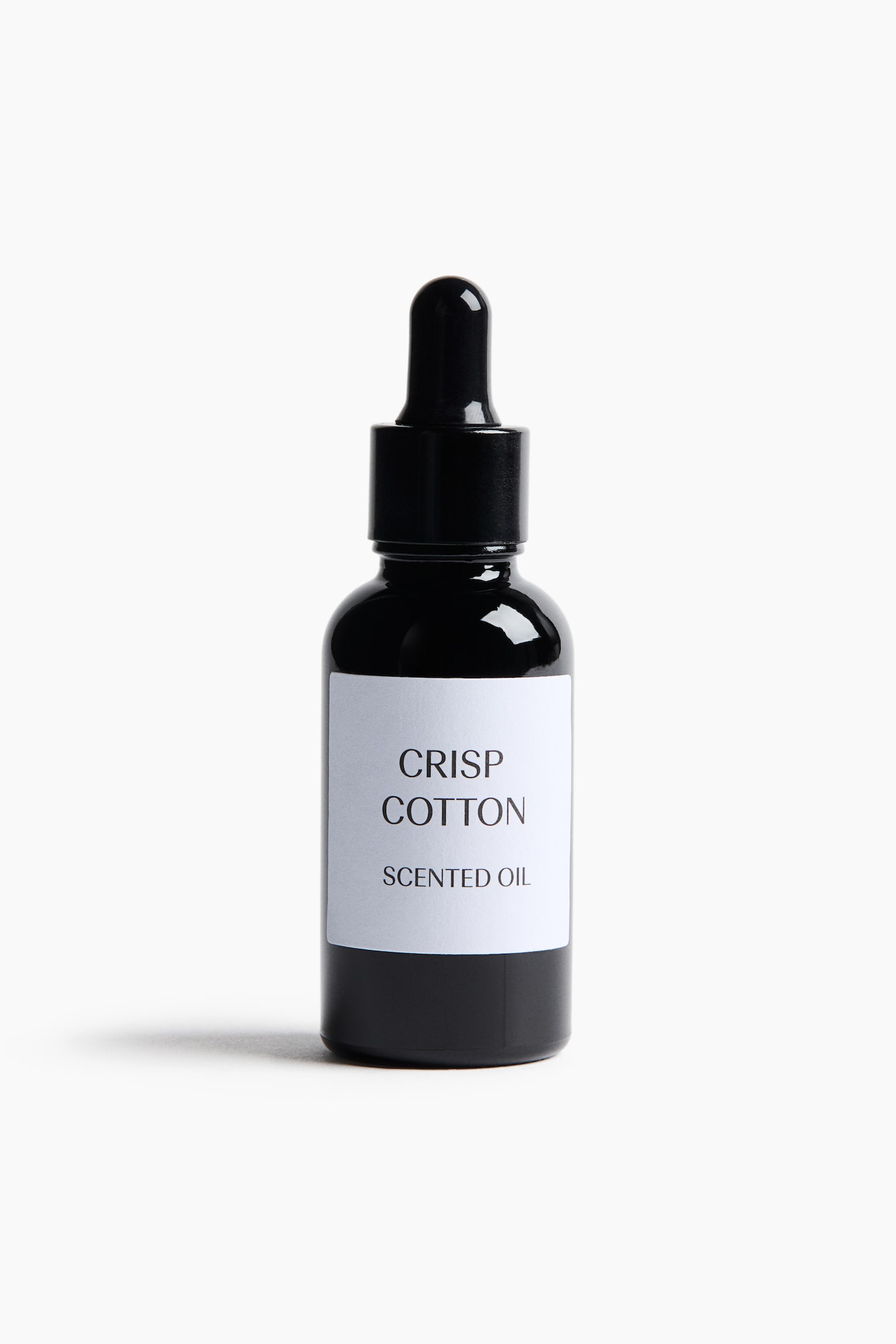 En sort glasdrÃ¥beflaske stÃ¥r oprejst og vender frontalt, med en hvid rektangulær etiket med den sorte tekst âCRISP COTTONâ og âSCENTED OILâ. Flasken har en sort skruelÃ¥g integreret med en drÃ¥betæller af gummibold. - 1