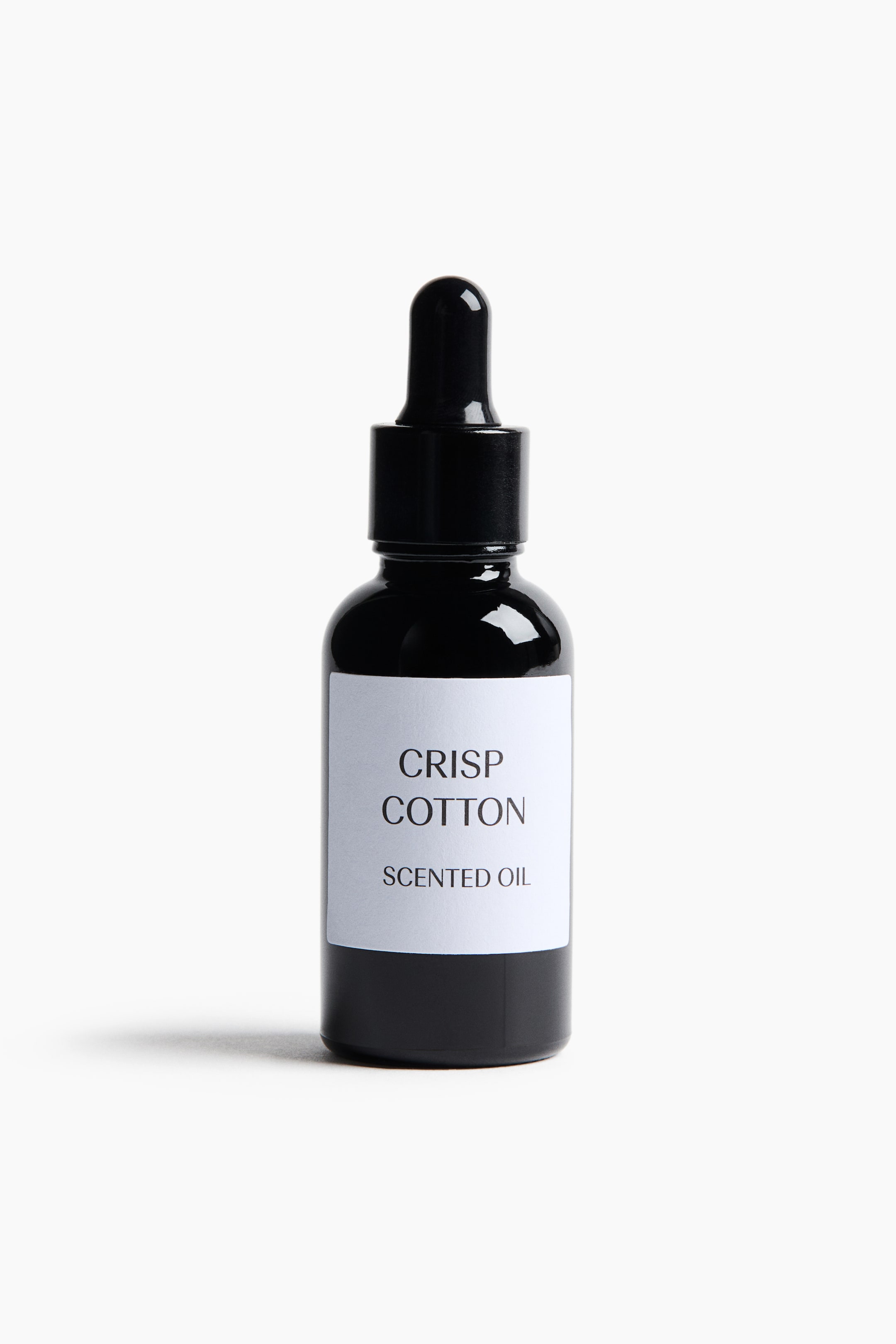 Näytä suurempi kuva: Musta lasinen pipettipullo seisoo pystyasennossa eteenpäin suunnattuna, ja siinä on valkoinen suorakulmainen etiketti, jossa on mustalla teksti "CRISP COTTON" ja "SCENTED OIL". Pullossa on musta kierrekorkki, johon on integroitu kuminen pipettipää.