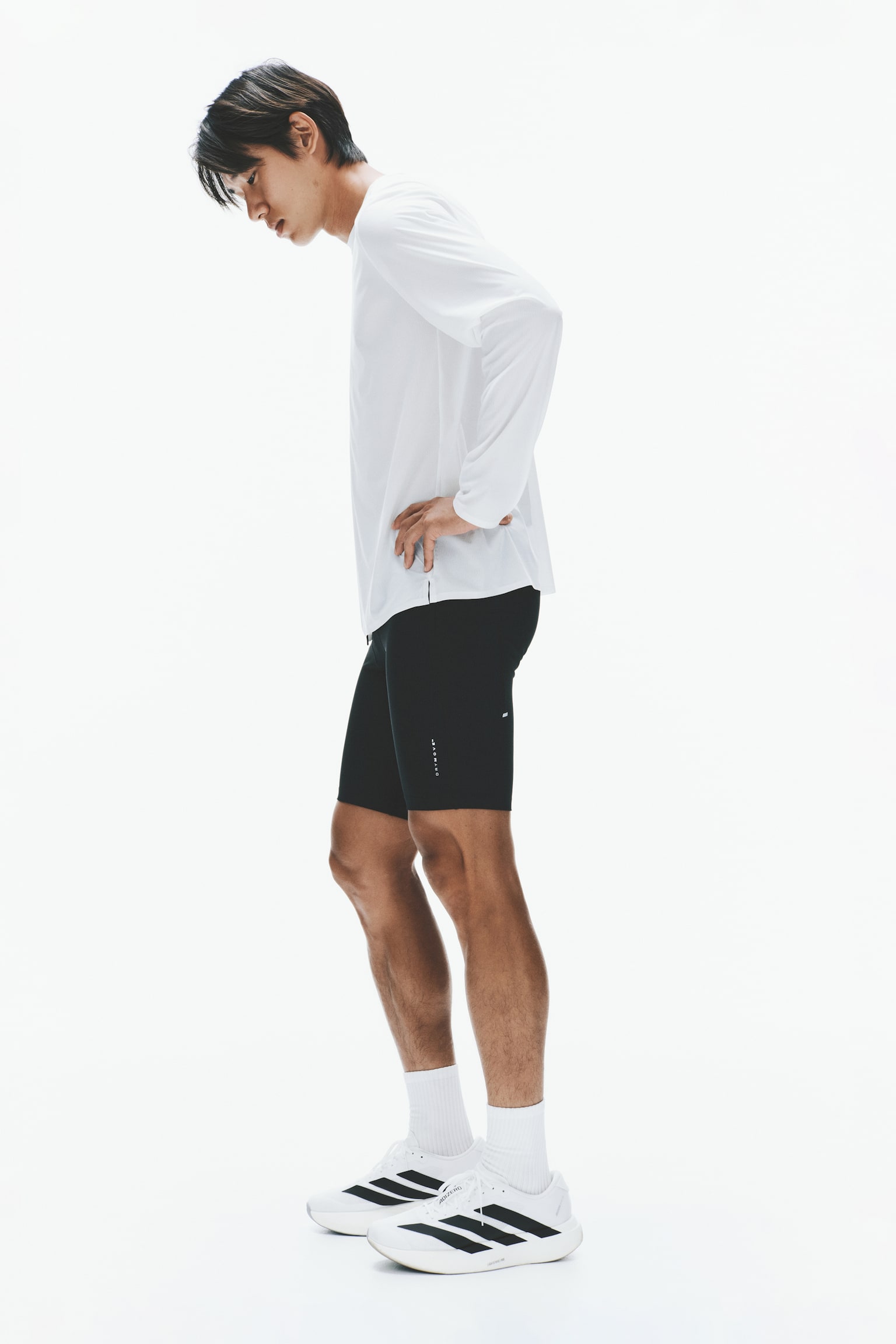 A white long-sleeved running top is shown from the front, featuring a crew neck and reflective strips on both shoulders. Small side slits are visible at the hem, and black "RUNNING M O V E" text is displayed on the inside collar band. - 1