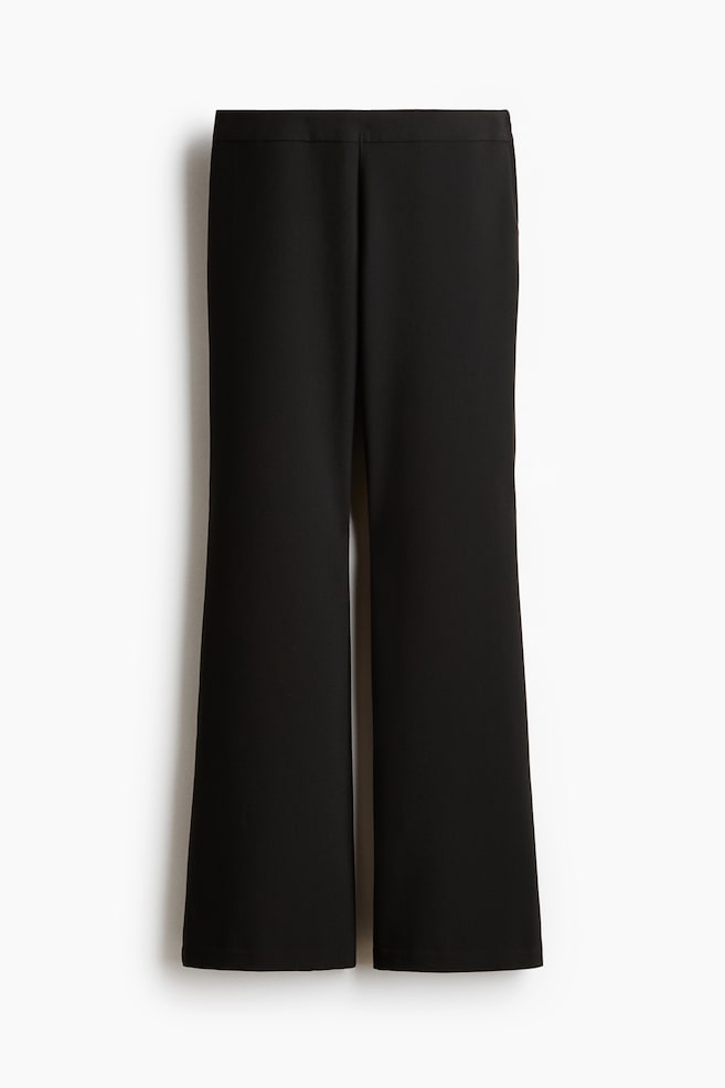 Pantalones negros con una pretina plana y una silueta de pierna ancha. El frente presenta un diseño limpio sin bolsillos ni cierres visibles, y las piernas se ensanchan desde la rodilla hacia abajo. - 1