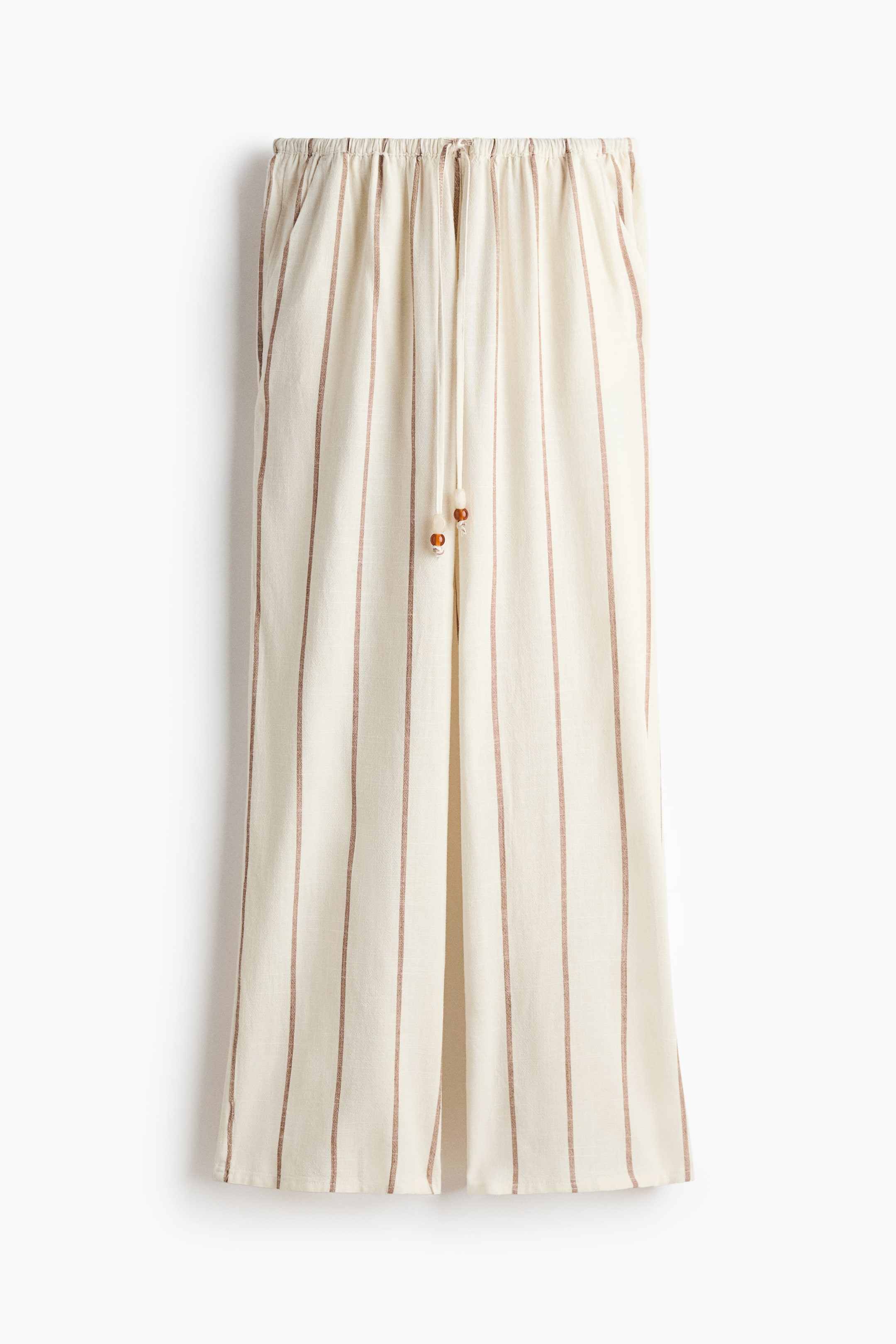 View larger image: These front-facing pants showcase a cream fabric adorned with narrow vertical reddish-brown stripes. They feature an elastic waistband with a drawstring, ending in two small wooden beads. Side pockets are located at the hips, highlighting a wide-leg cut.