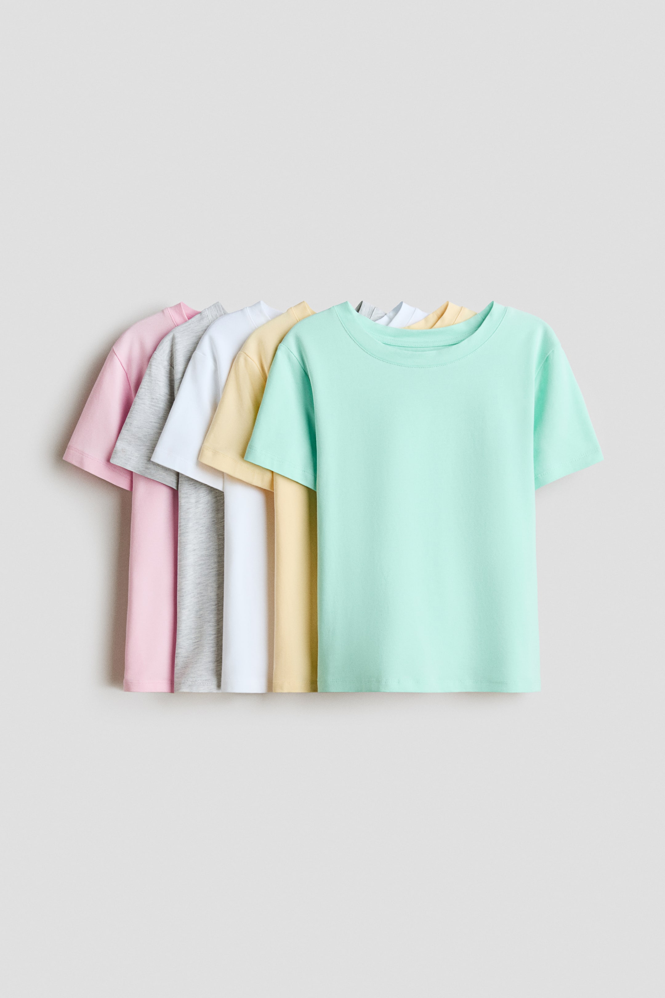 View larger image: Five cotton jersey T-shirts are arranged in an overlapping row facing forward, showcasing a mint green T-shirt in the foreground, followed by pastel yellow, white, heather grey, and light pink T-shirts. Each T-shirt features a round crew neckline with a narrow trim and short sleeves.