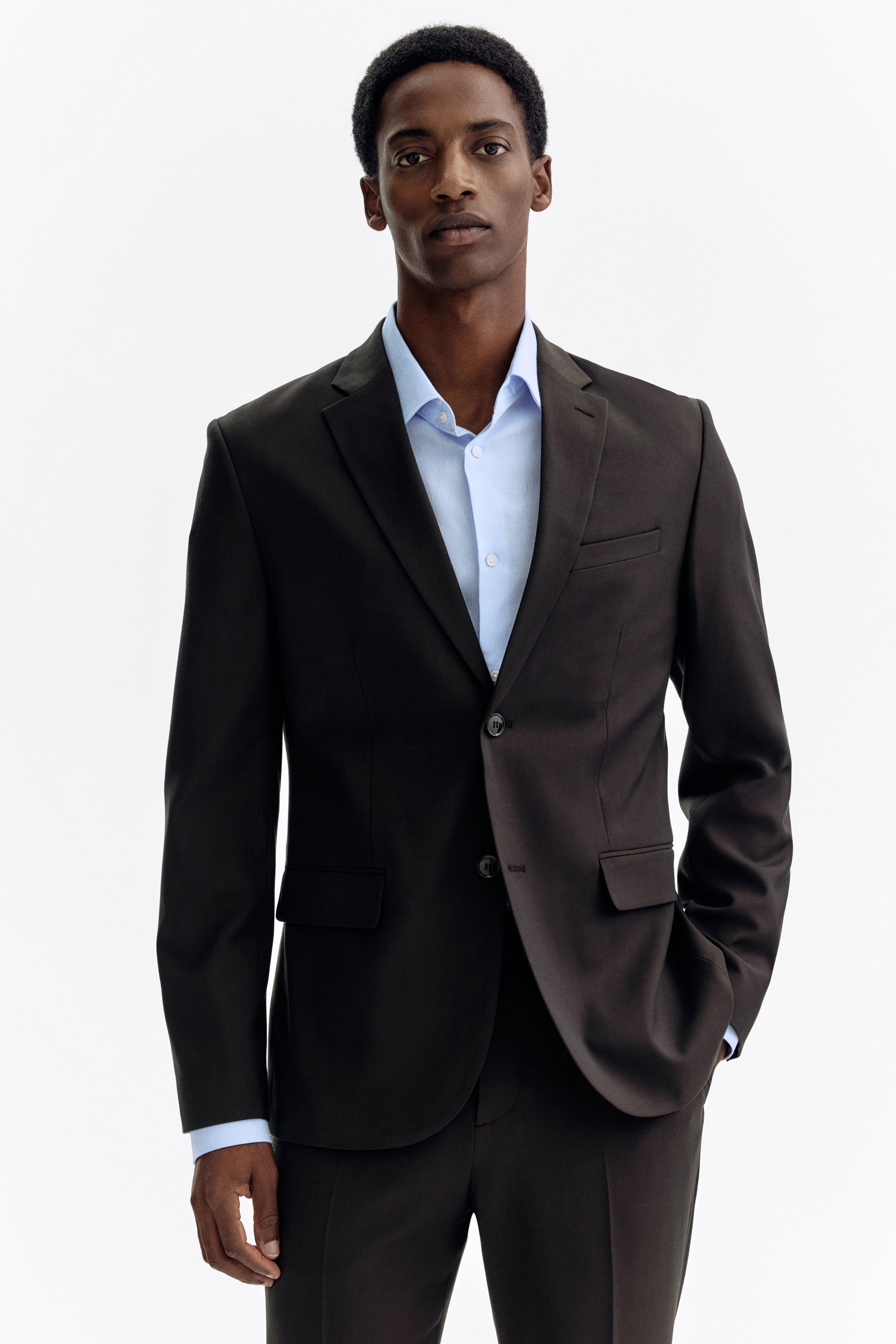 View larger image: Presenting a dark brown suit, showcasing a single-breasted jacket with notch lapels, a two-button closure, a welt chest pocket, and two flap pockets. The jacket is paired with a light blue collared shirt, complemented by matching trousers.