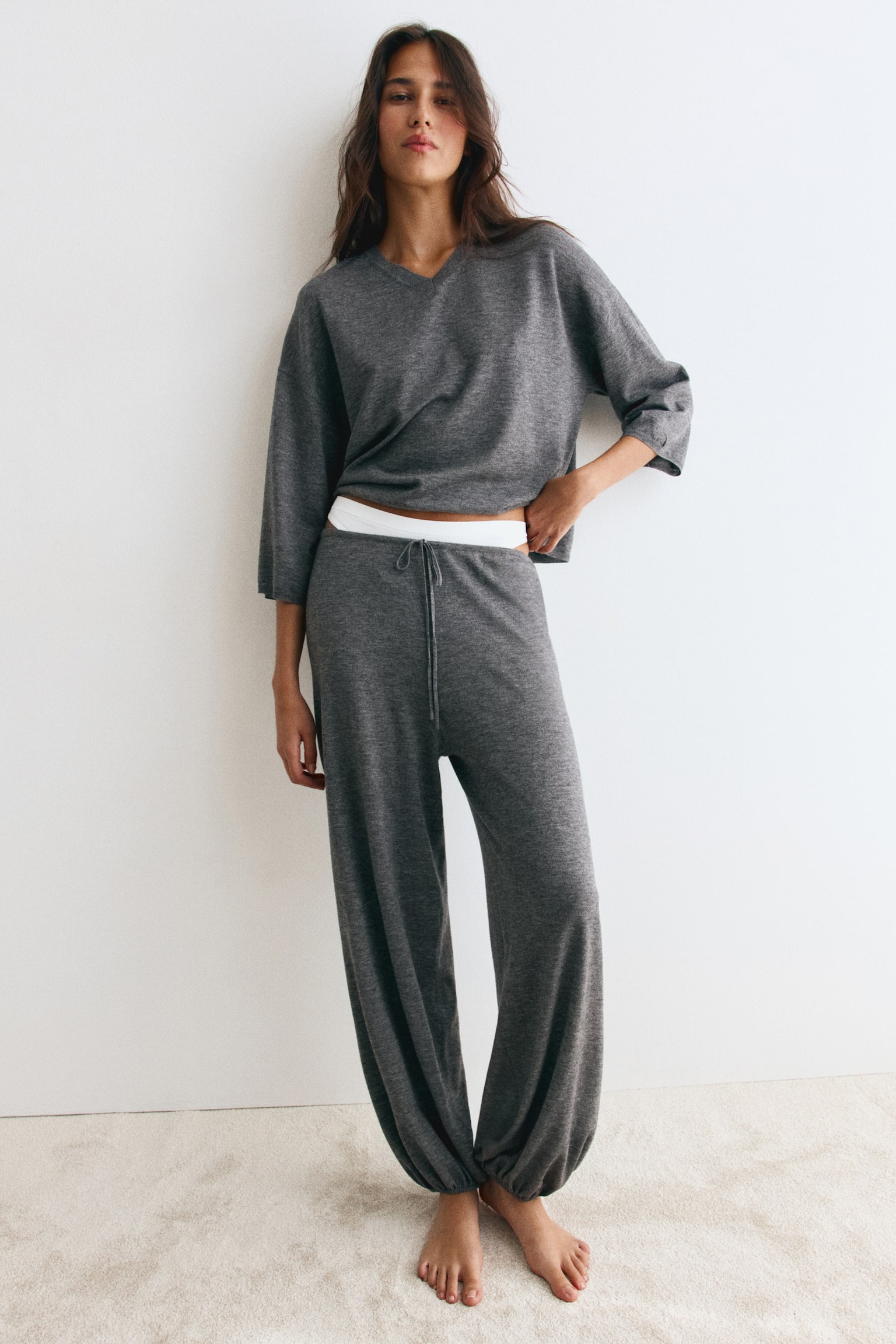 Grey wool-blend knit joggers featuring an elasticated drawstring waist and loose balloon legs with elasticated ankle hems are worn by the model. The joggers are paired with a matching grey knit top, with a white waistband visible underneath. - 1