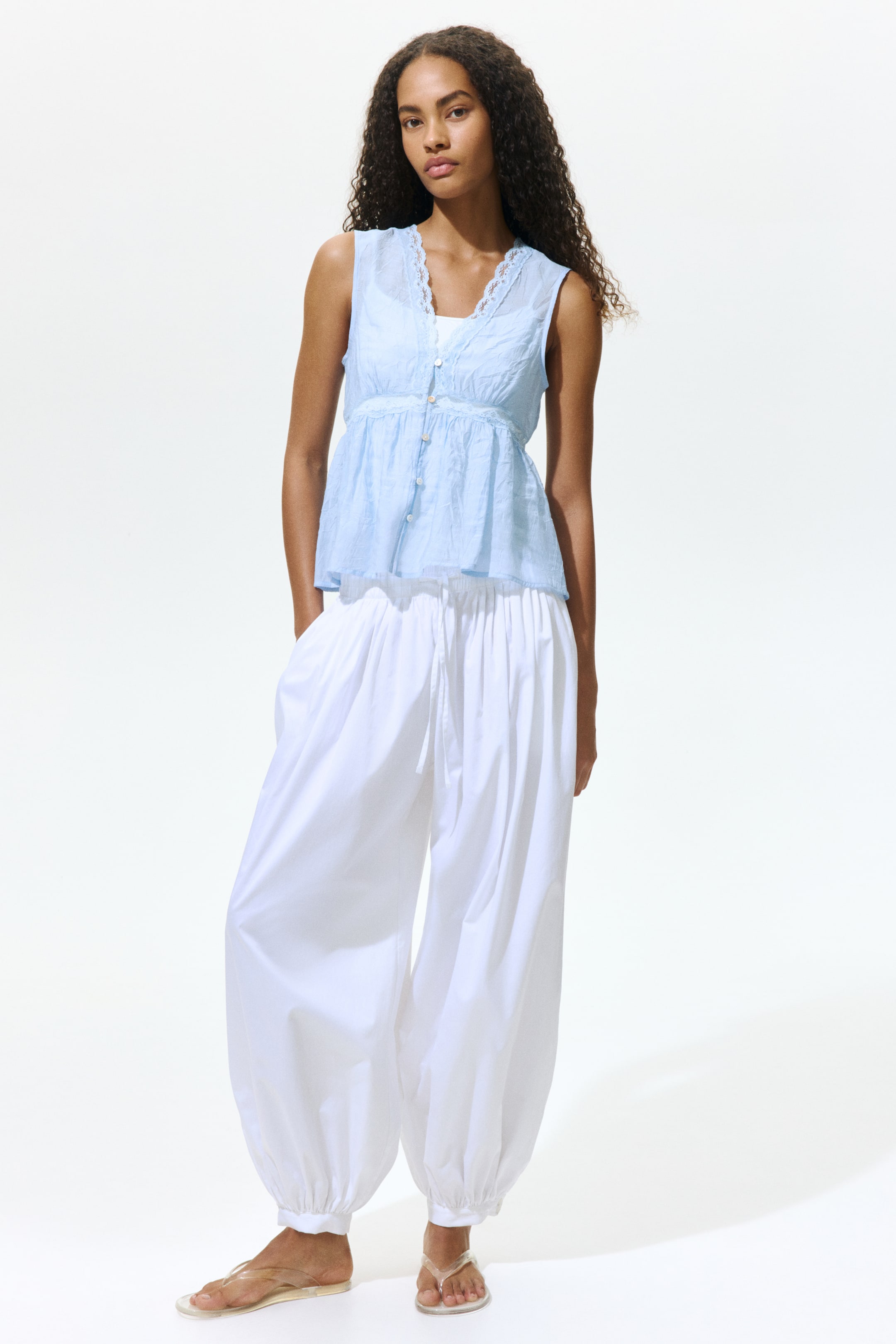 View larger image: A light blue sleeveless top in viscose-blend poplin is worn by the model over a white camisole. The top showcases a lace-trimmed V-neckline and buttons running down the front, with a lace inset situated under the bust and gathers below that create a gently flared peplum.