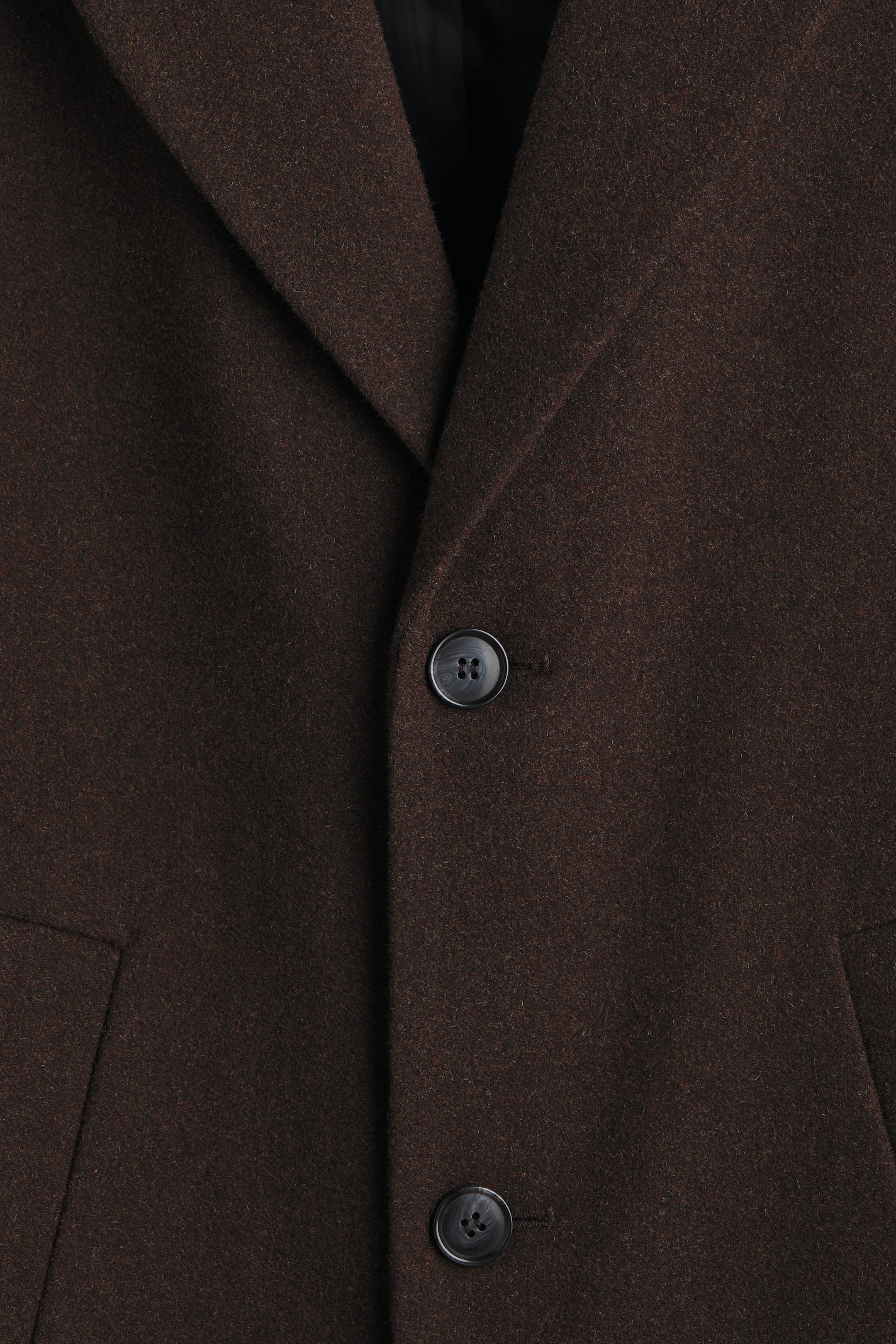 View larger image: A dark brown coat is presented FRONT, featuring a folded notch lapel revealing a dark lining. Two round, dark buttons with a textured finish are visible on the front closure, positioned above a horizontal flap pocket. The fabric has a subtly textured appearance.