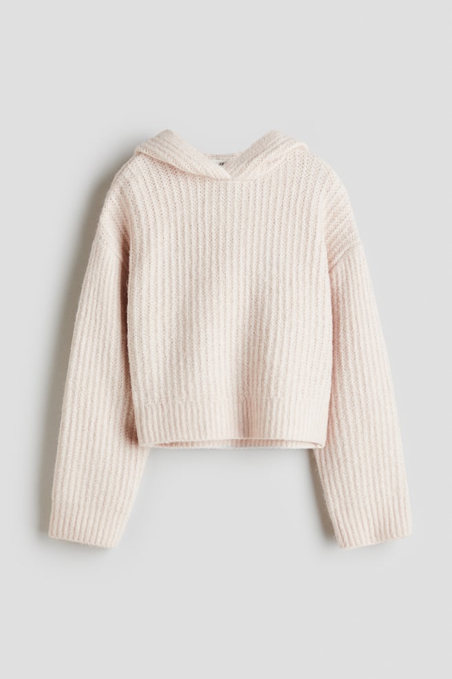 A front-facing, light pink loose-fit hoodie is displayed, featuring a soft rib knit. It has a hood with a wrapover front, dropped shoulders, long sleeves with ribbed cuffs, and a cropped hem. - 1