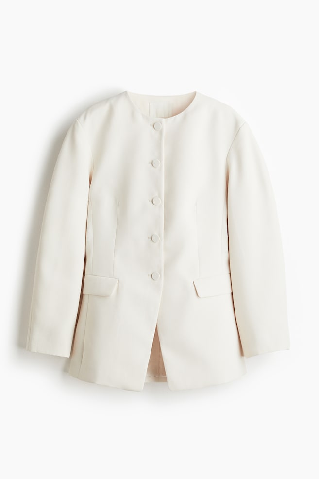 A cream jacket is presented from the front, featuring a round collarless neckline. It has a central button closure with four buttons and two flap pockets, one on each side. - 1