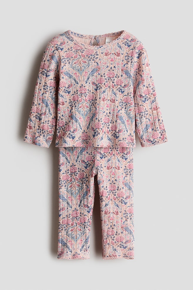 A front-facing view shows a two-piece top and leggings set in pink ribbed cotton jersey featuring an all-over floral and bird print in shades of blue and pink. The long-sleeved top has a round neckline with delicate picot trim, while the matching leggings feature similar picot-trimmed ankle cuffs. - 1