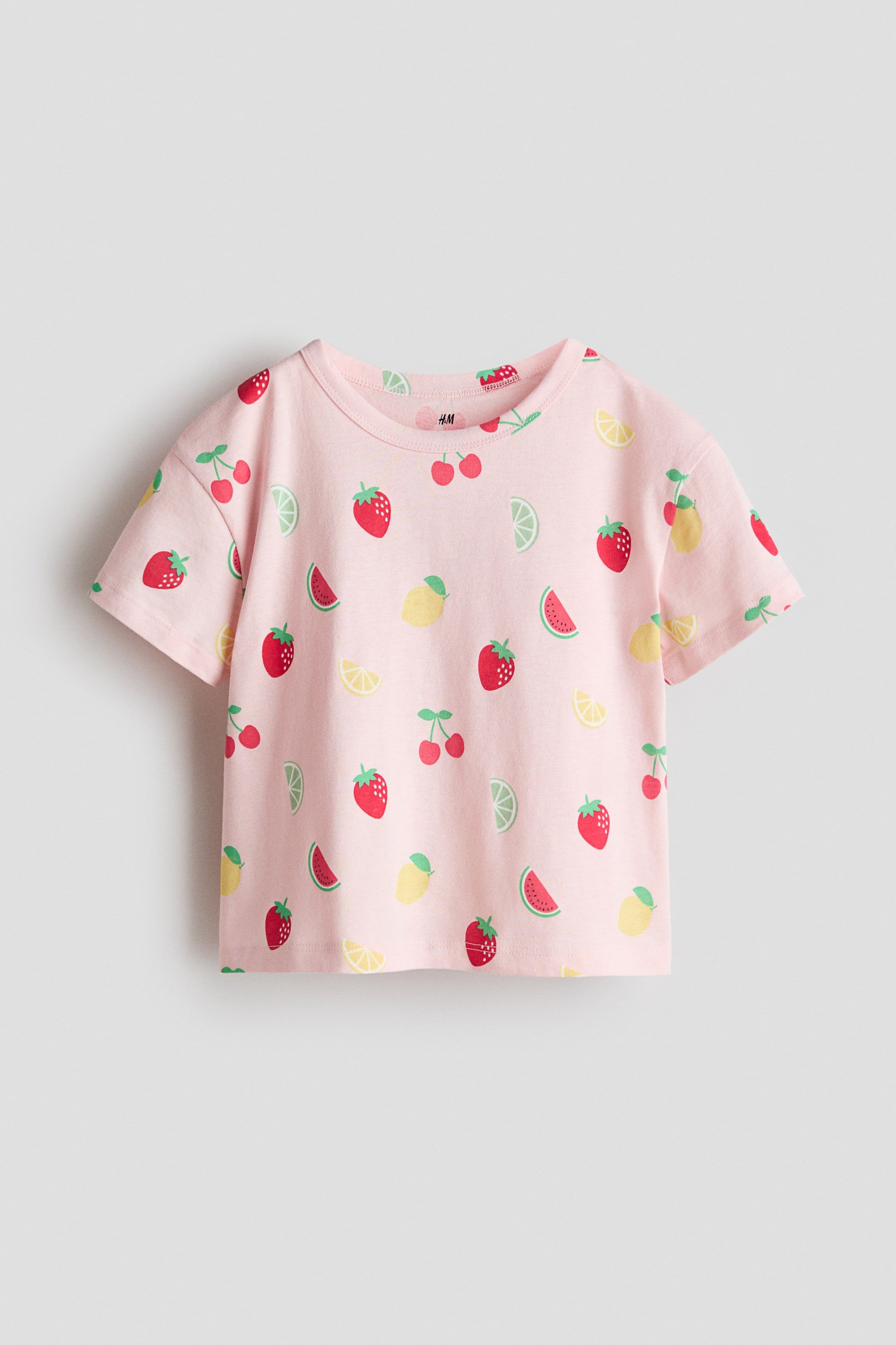 View larger image: A pink t-shirt is showcasing its front, adorned with an allover pattern of red strawberries, red cherries, green watermelon slices, yellow lemon slices, and green lime slices. It is crafted with a round neck and short sleeves.