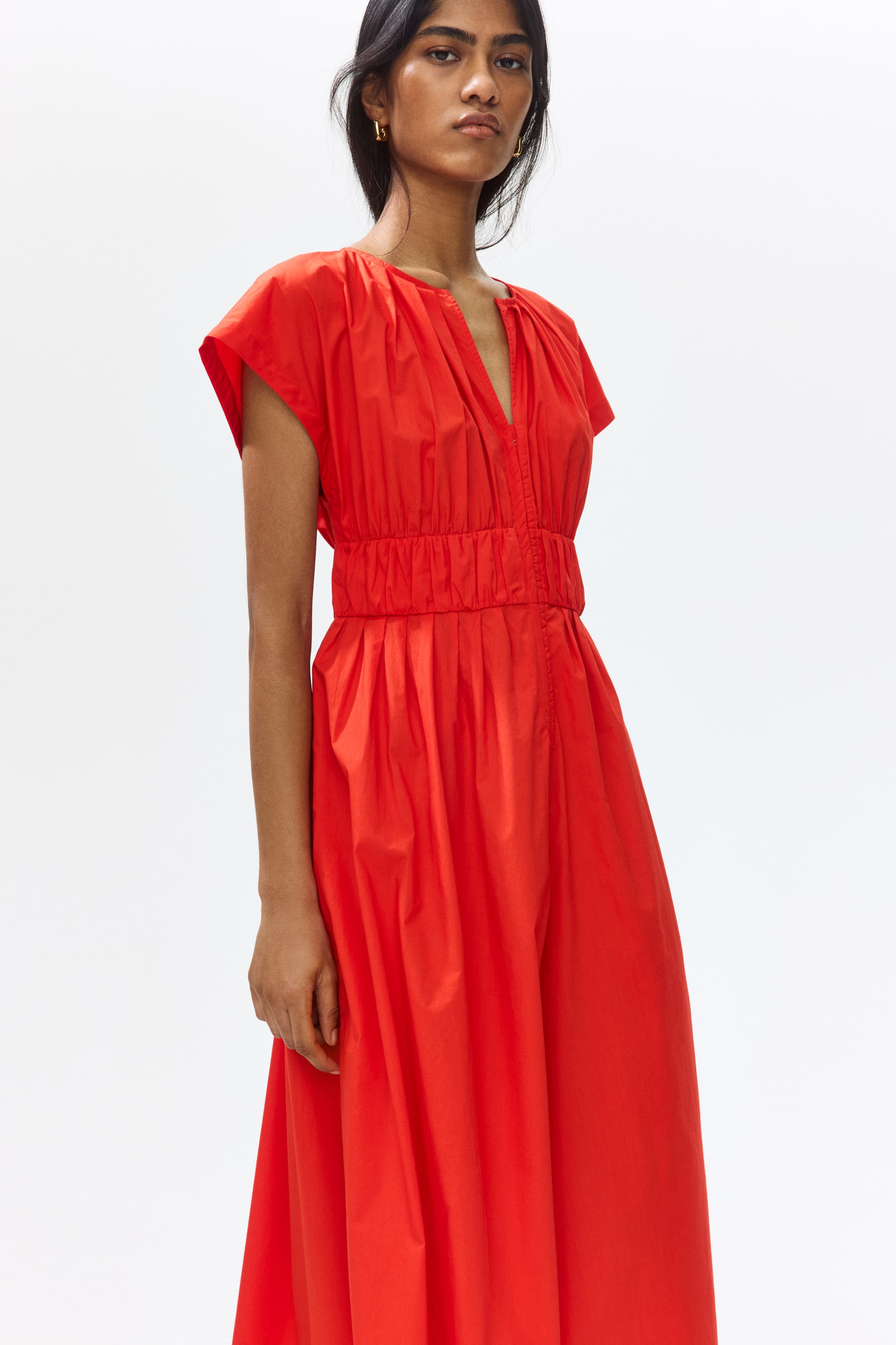 View larger image: The model is showcasing a red calf-length dress. It boasts a round neckline with pleats, a V-shaped front opening, cap sleeves, and gathered seams below the bust, crafting a nipped-in silhouette.
