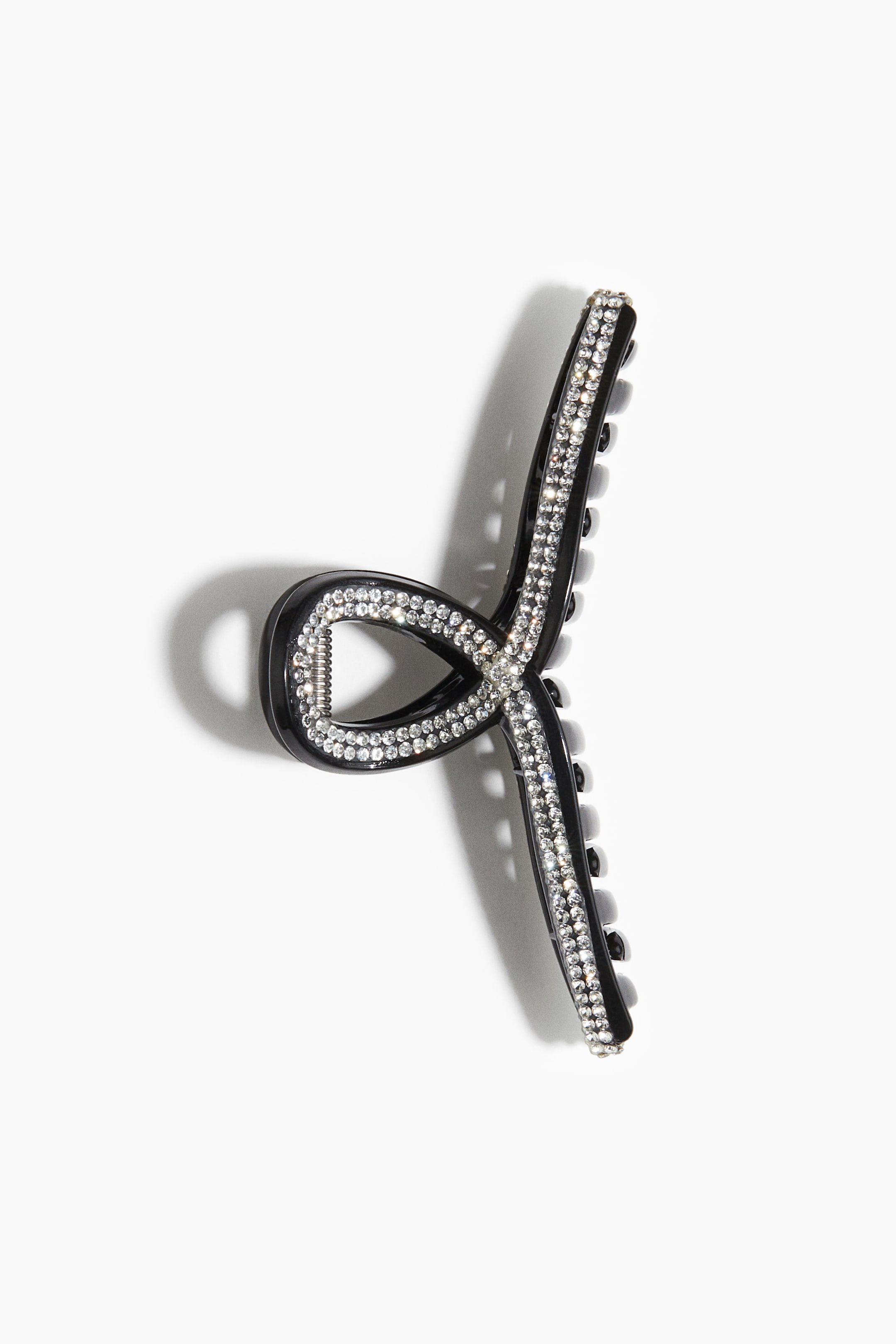 View larger image: A black hair claw clip is showcasing two curved top arms that are intersecting to form an X-shape. Clear rhinestones are detailing the outer edges of these arms and their central intersection.
